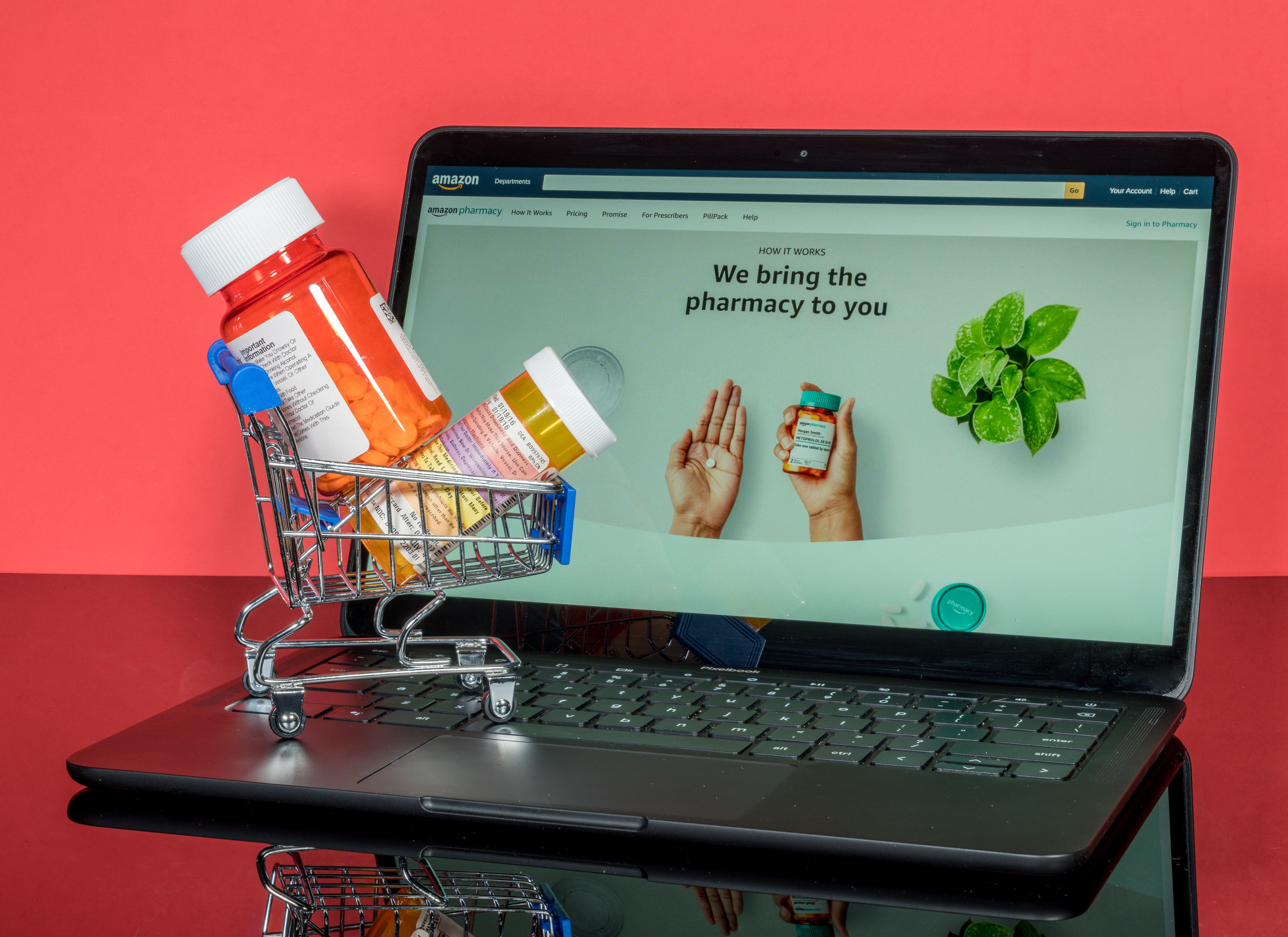 Mini shopping cart with pill bottle on laptop showing Amazon Pharmacy | Image Credit: © steheap - stock.adobe.com