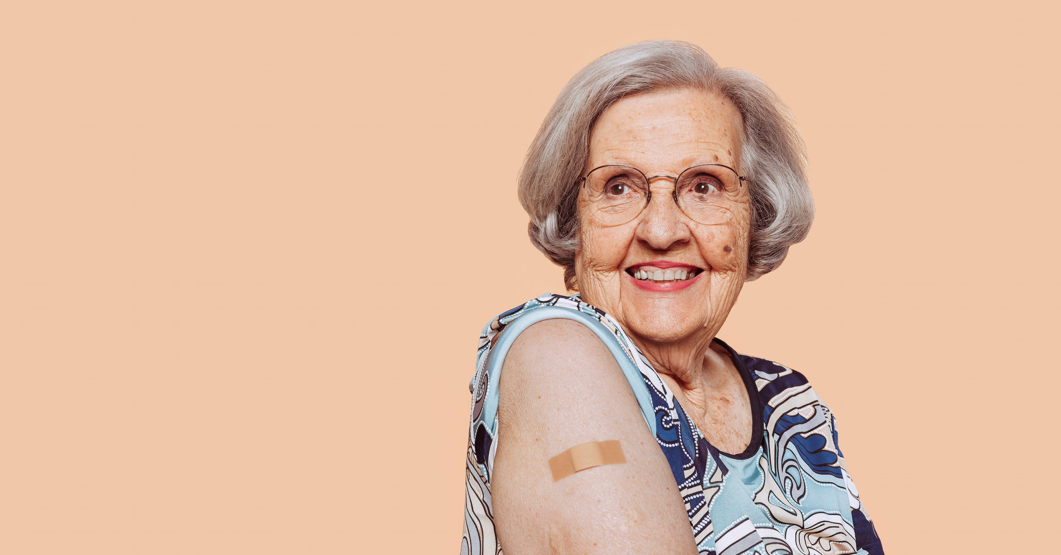 Portrait of a smiling elderly grandmother after receiving a vaccine. Elder woman showing her bandaged arm after receiving vaccination.