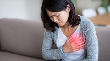 Woman holding chest in pain, experiencing discomfort, possible cardiac issue, sitting on a couch.
