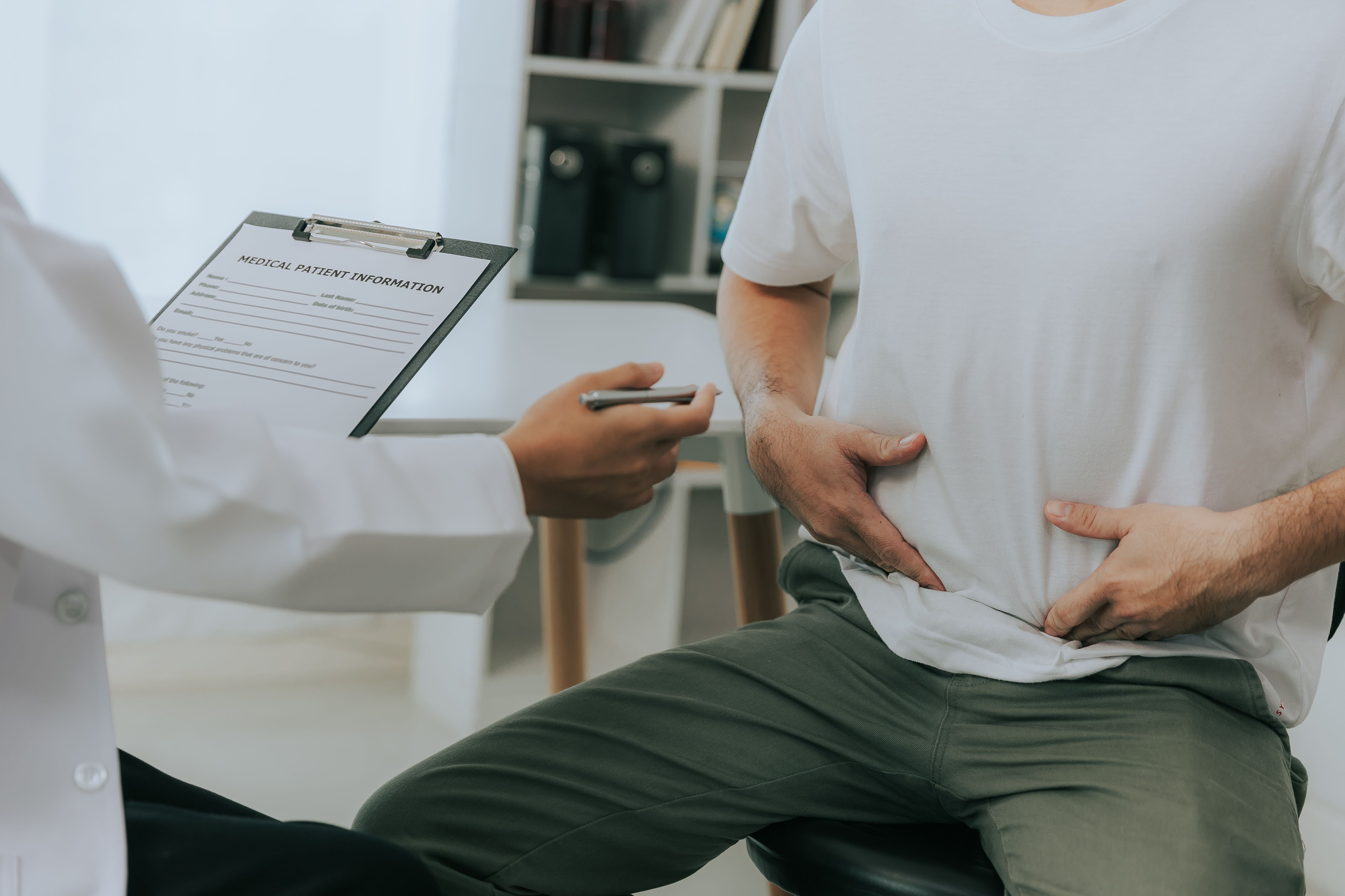 Crohn disease or ulcerative colitis concept. Doctor counseling male patient with abdominal pain in hospital examination room - Image credit: Witoon | stock.adobe.com