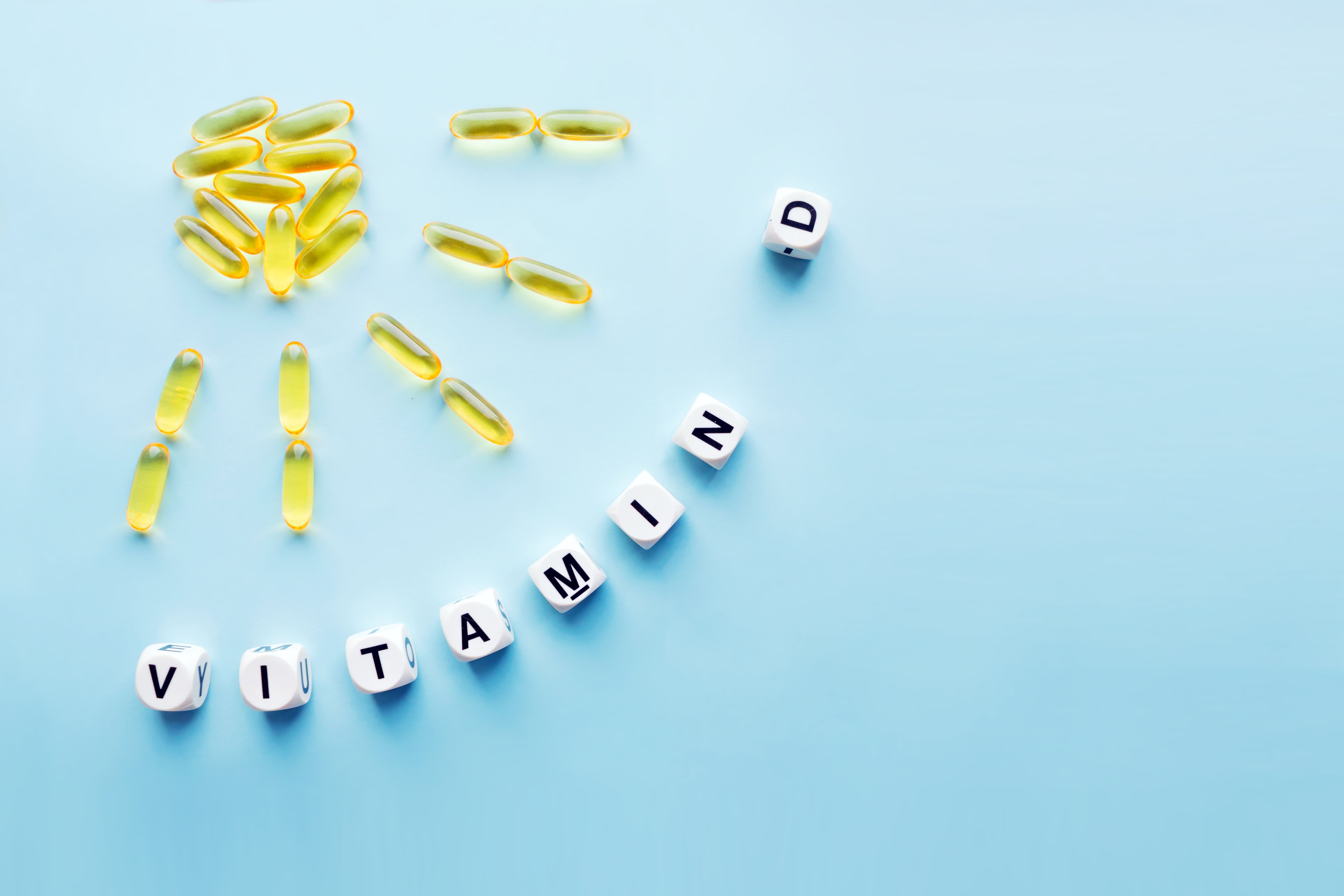 Yellow capsules in the form of the sun with rays and the word vitamin D from white cubes with letters on a blue background. VITAMIN D word for healthy | Image Credit: © irissca - stock.adobe.com