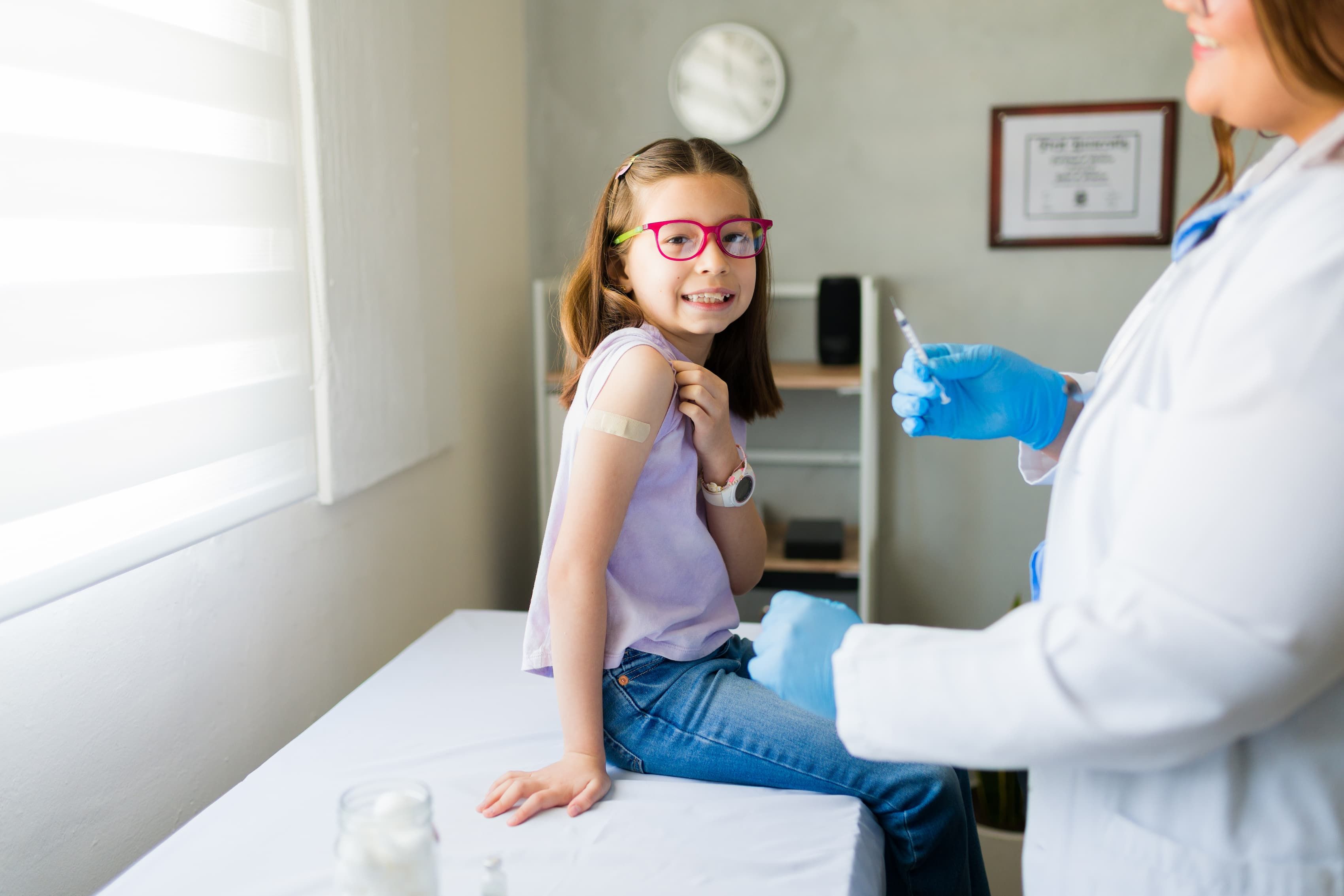 Young girl smiling after receiving a vaccine from a pediatrician in a doctor's office, showing confidence and healthcare Young girl smiling after receiving a vaccine from a pediatrician in a doctor's office, showing confidence and healthcare