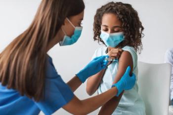 A medical worker is giving a Covid-19 vaccination to a young girl in a clinic indoors. Both are wearing face masks for safety during the antiviral immunization. | Image Credit: Prostock-studio | adobe.stock.com