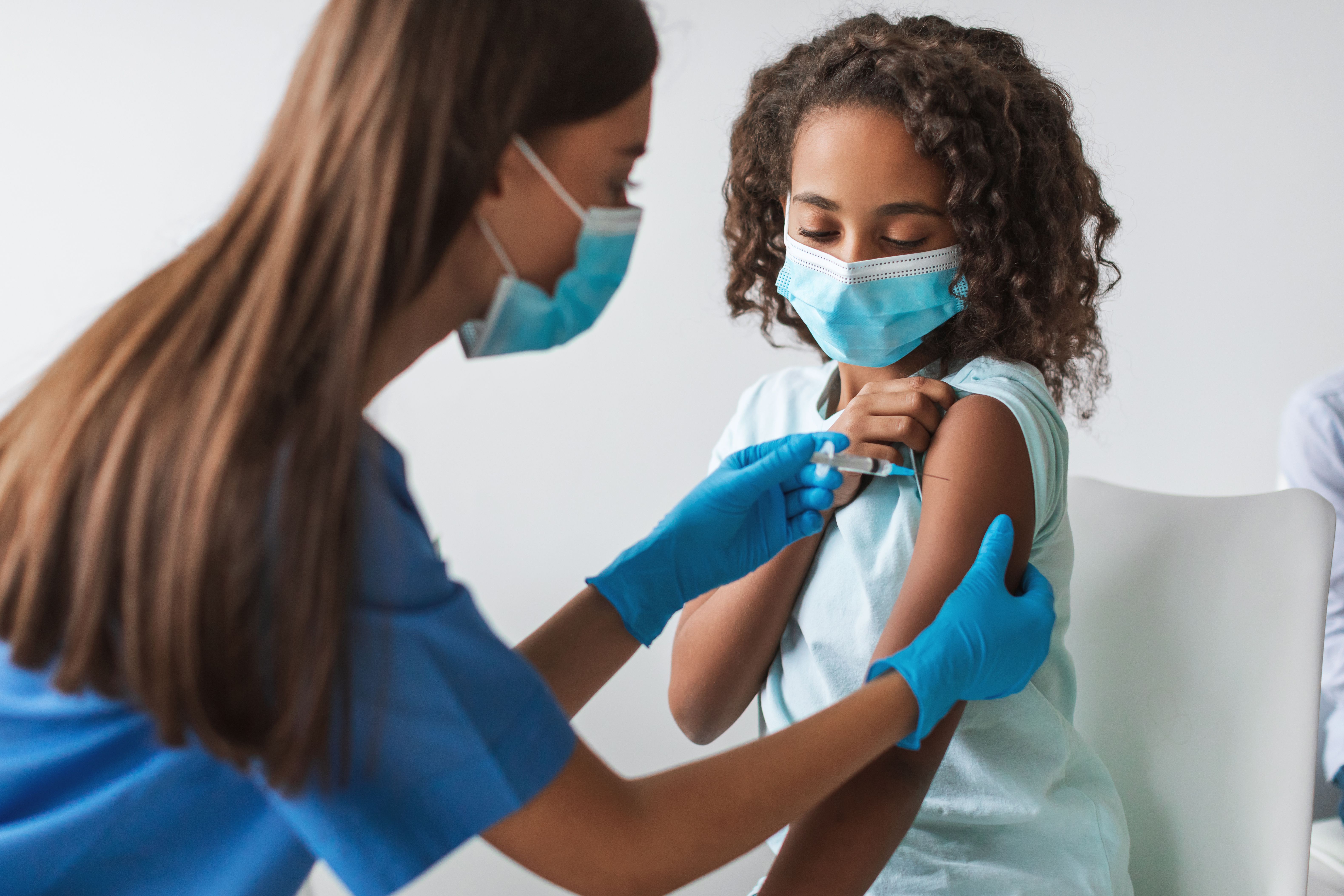 A medical worker is giving a Covid-19 vaccination to a young girl in a clinic indoors. Both are wearing face masks for safety during the antiviral immunization. | Image Credit: Prostock-studio | adobe.stock.com A medical worker is giving a Covid-19 vaccination to a young girl in a clinic indoors. Both are wearing face masks for safety during the antiviral immunization. | Image Credit: Prostock-studio | adobe.stock.com