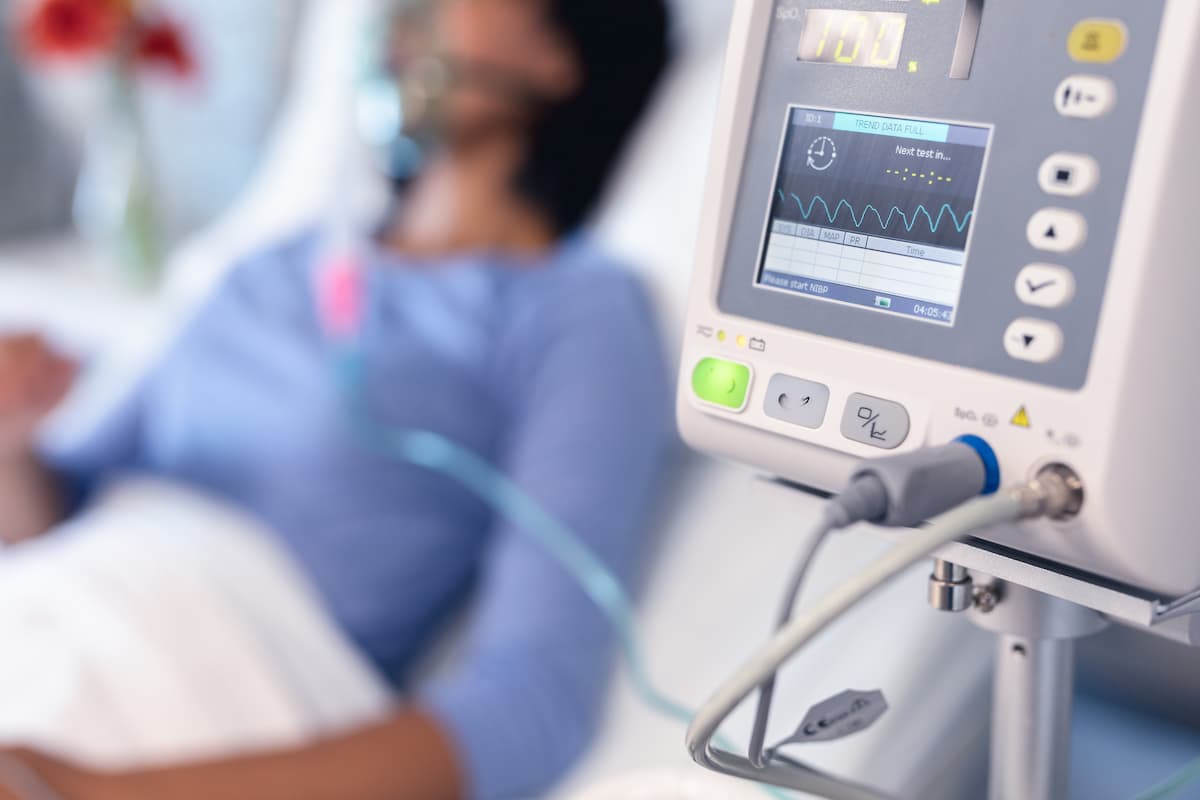 Ventilator monitor and african american female patient in hospital bed with oxygen ventilator