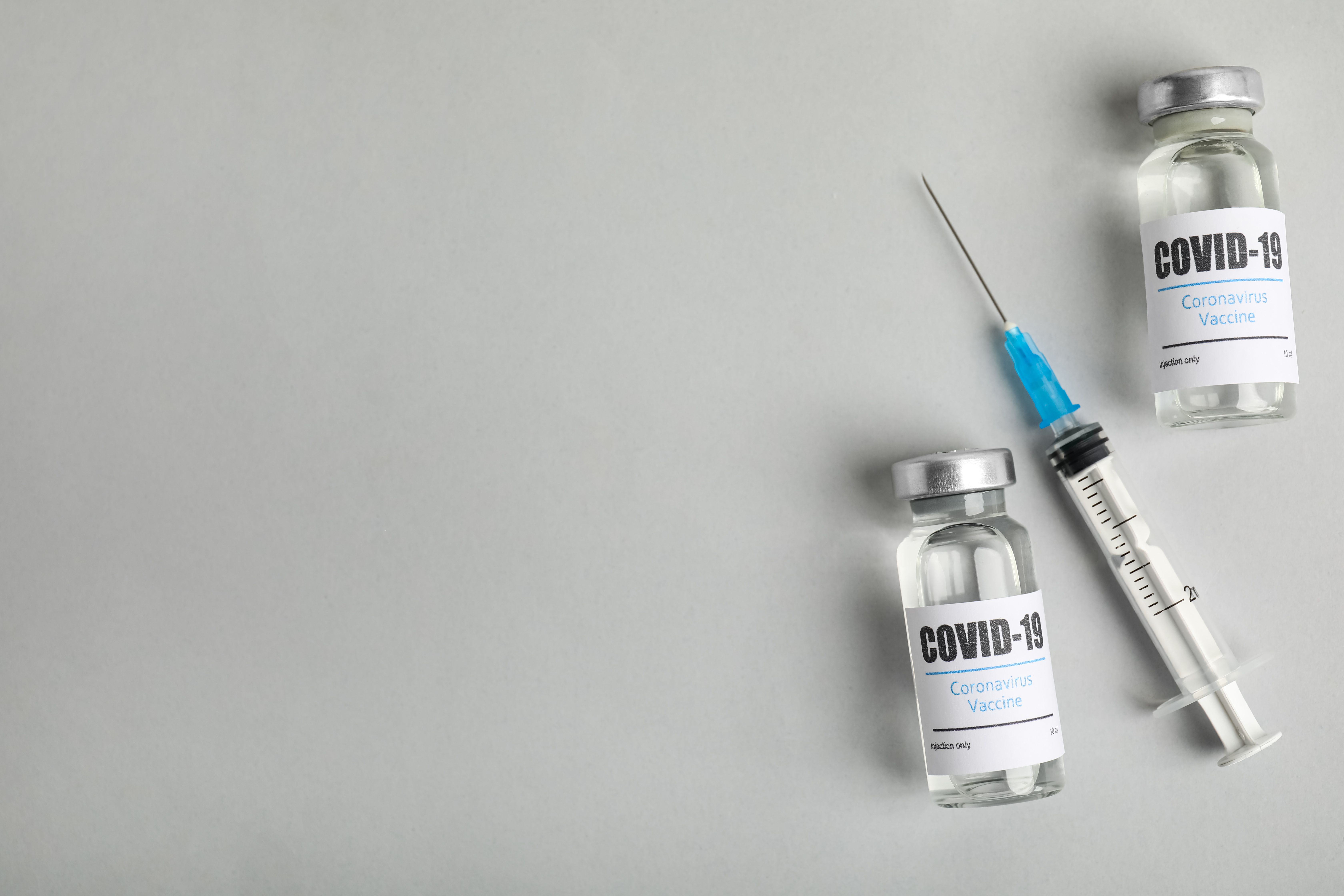 Vials with coronavirus vaccine and syringe on light background, flat lay - Image credit: New Africa | stock.adobe.com