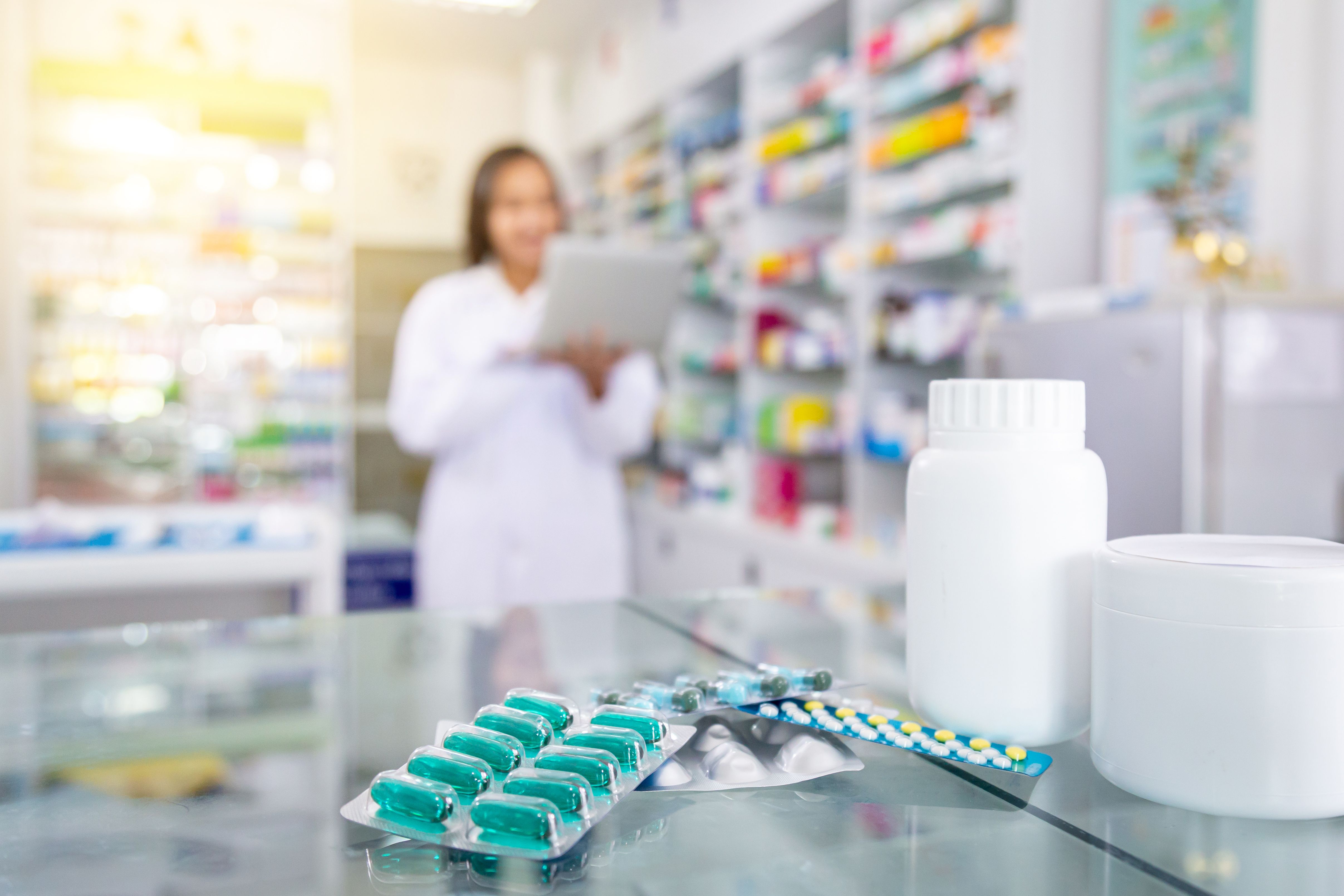 Capsules medicine and white medicine bottles on table in drugstore with blurred background of pharmacist and pharmacy. | Image Credit: Satawat - stock.adobe.com