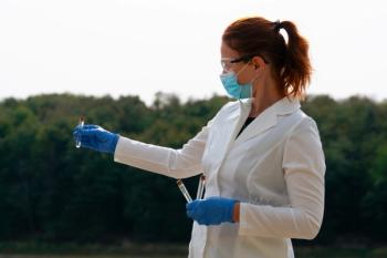 pneumonic plague outbreak scientist holding test tube sample, focused female epidemiologist in lab coat, face mask and blue gloves examining sample looking away from camera, forest and sky