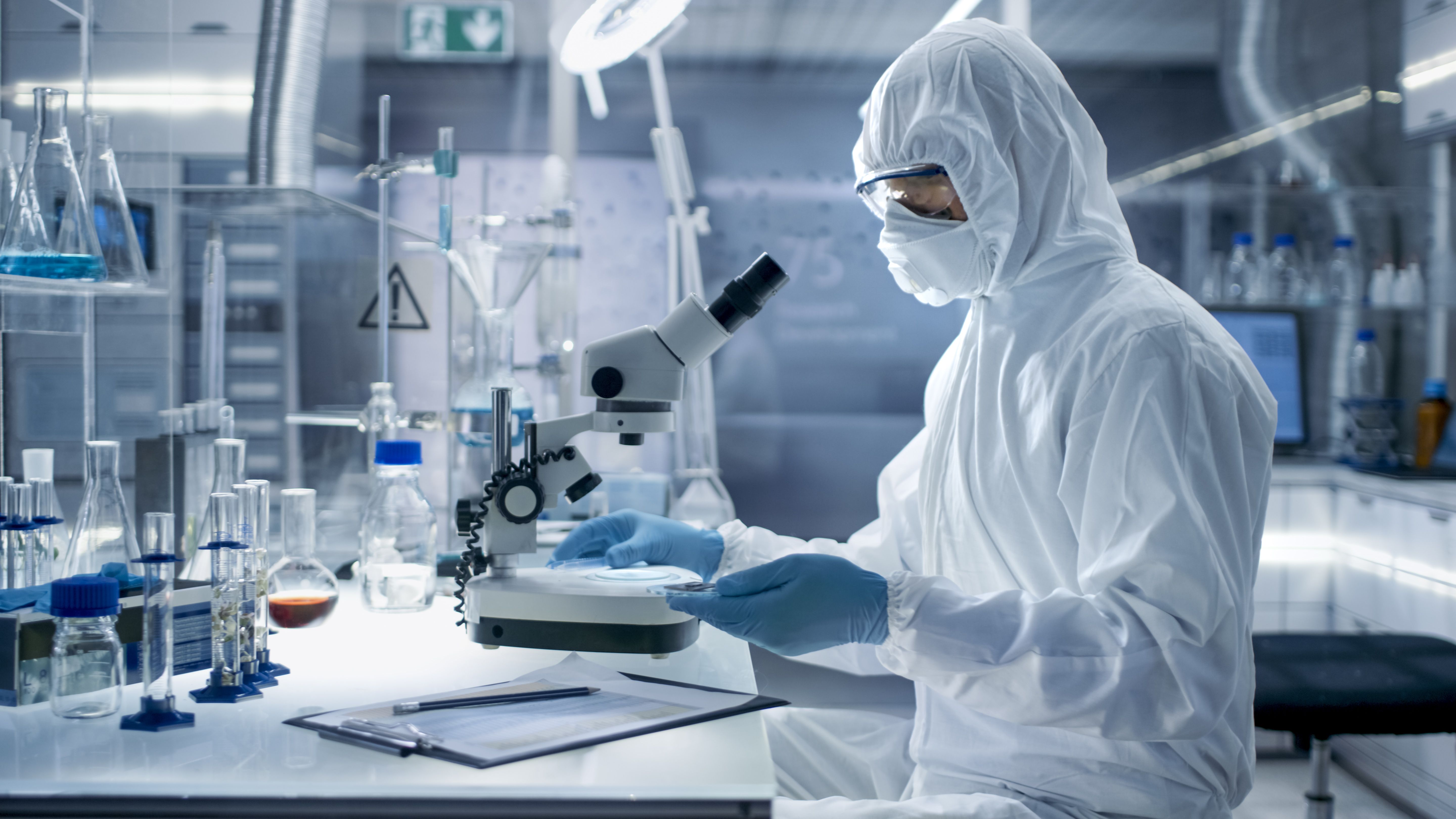 In a Secure High Level Laboratory Scientists in a Coverall Conducting a Research. Chemist Adjusts Samples in a Petri Dish with Pincers. | Image Credit: Gorodenkoff | stock.adobe.com