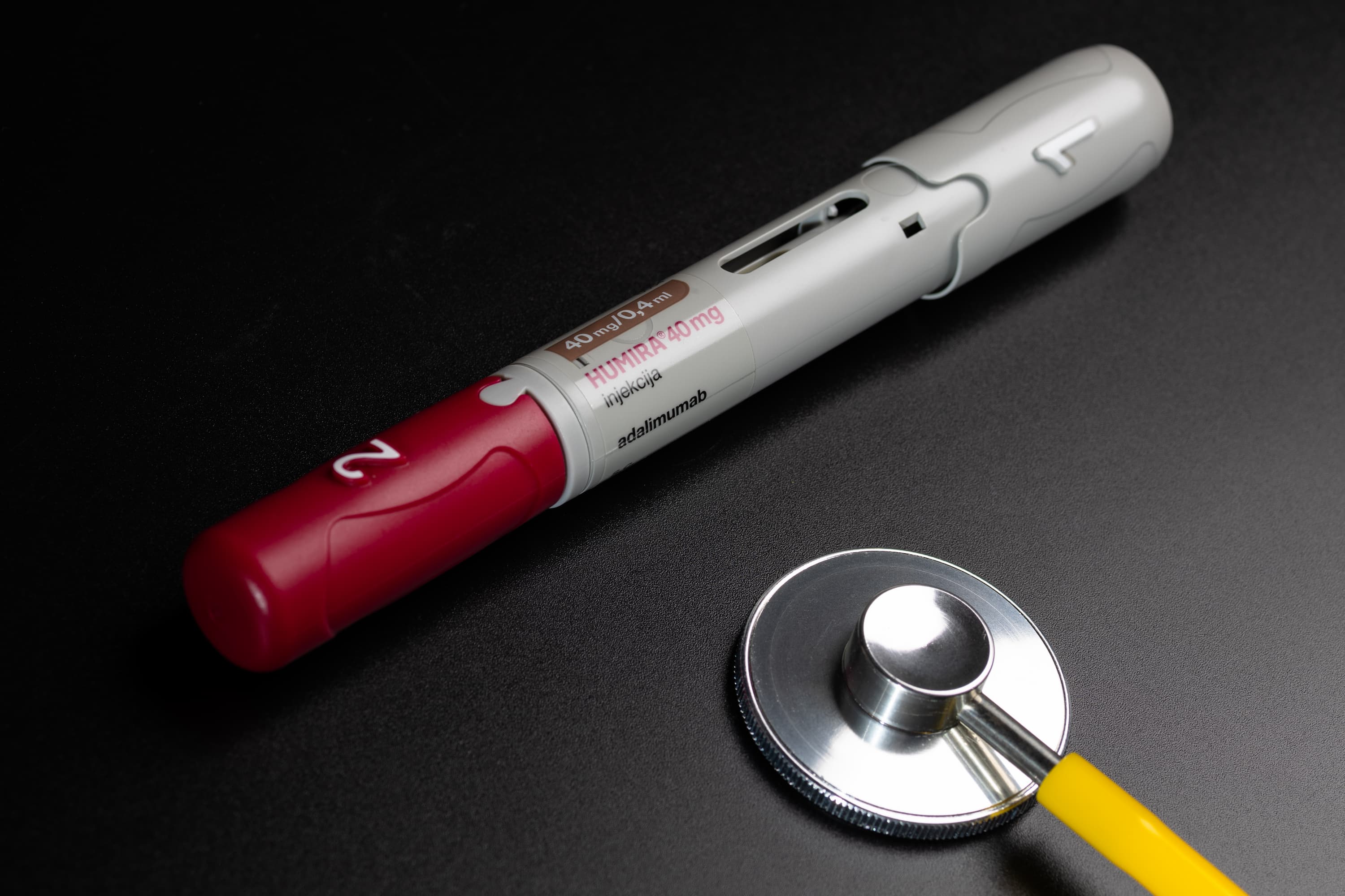 Humira Injection Pens Arranged With Stethoscope on Black Background in Dark Studio Lighting
