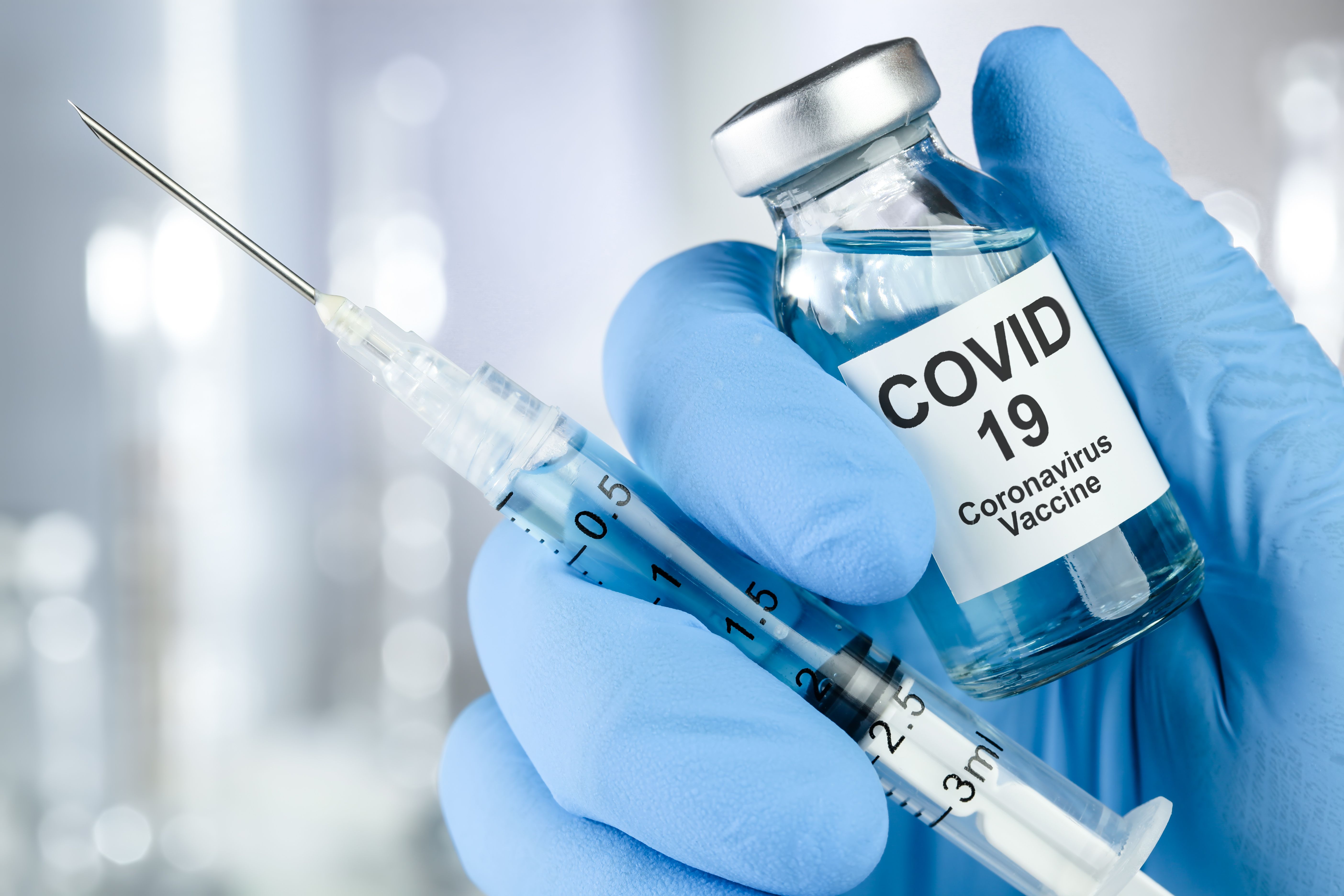 Healthcare cure concept with a hand in blue medical gloves holding Coronavirus, Covid 19 virus, vaccine vial - Image credit: Leigh Prather | stock.adobe.com