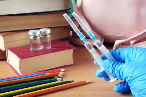 bottles and syringes of vaccine aganist covid-19 near book pile and school supplies, back to school in coronavrus time concept - Image credit: lesslemon | stock.adobe.com