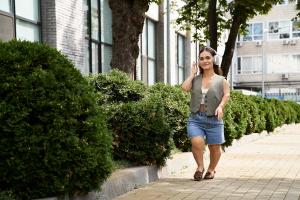 A cheerful brunette young woman with short stature strolls along a path lined with vibrant greenery, embracing the sunny day outdoors.