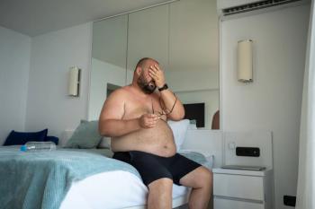 Tired obese man sitting put hand on head feeling unwell indoor. Endocrine disorders in body, lack of sleep as result of overweight in heavy man. Hypertension, diabetes mellitus, chronic heart failure