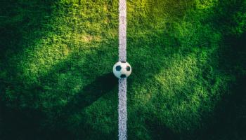 Soccer ball on the white touchline of a green football field at stadium under bright sunlight, perfect for sports training, match competition, or athletic championship | Image Credit: © ณัฐพล ตีระพิมลจันทร์ - stock.adobe.com