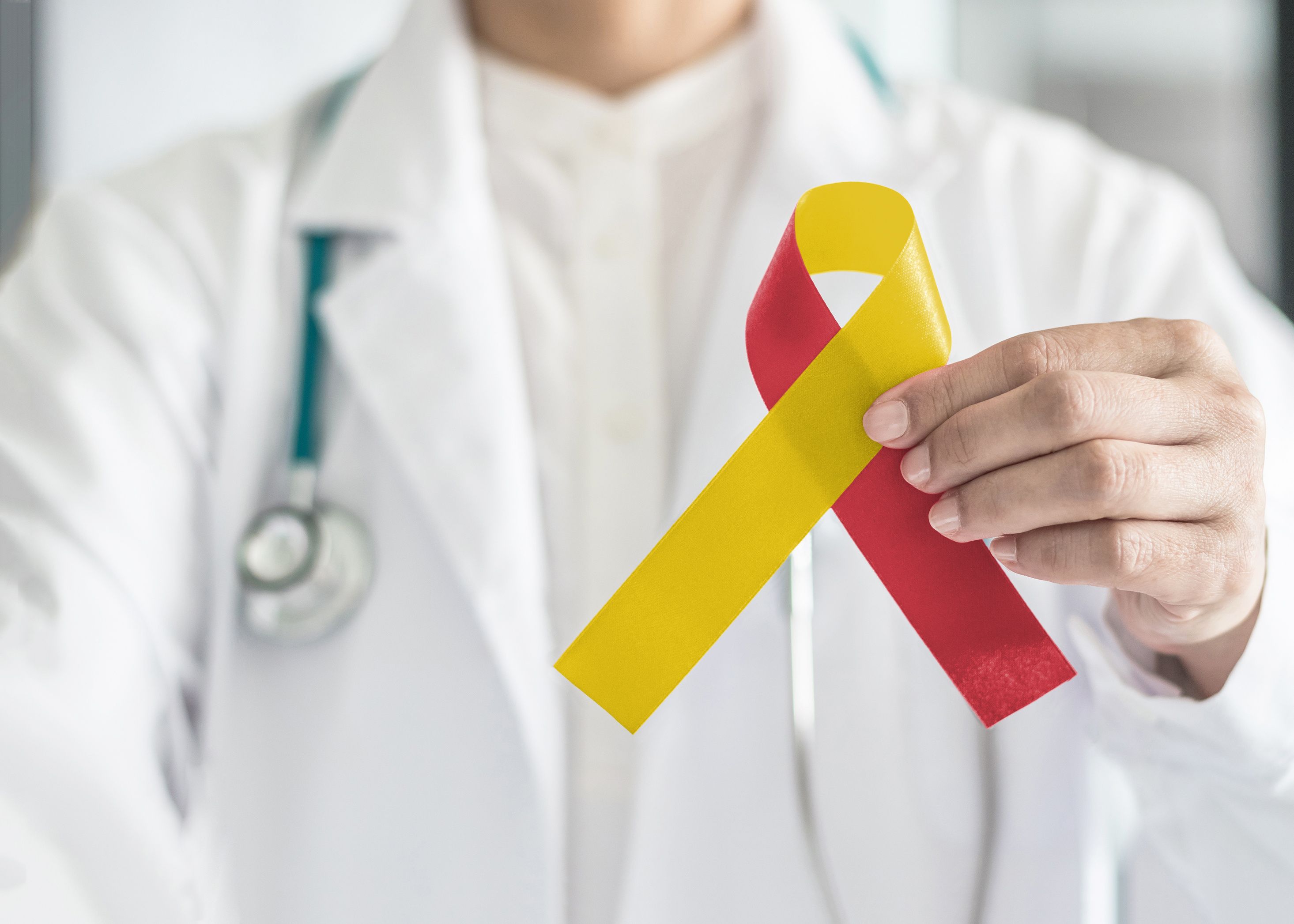 World hepatitis day and HIV/ HCV co-infection awareness with red yellow ribbon in medical doctor hand symbolic bow color to support patient with illness and hepatic disease | Image credit: Chinnapong - stock.adobe.com