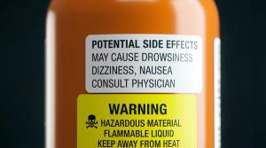 Close up on an orange pharmaceutical or chemical container label showing potential side effects and warning information like hazardous material and flammable liquid warnings warning label | Image Credit: Norah Allen | stock.adobe.com
