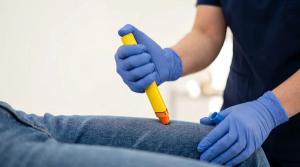 Close up of hands in blue medical gloves administering an epinephrine auto injector epipen shot into the outer thigh of a patient wearing jeans during an allergic emergency - Image credit: solom | stock.adobe.com