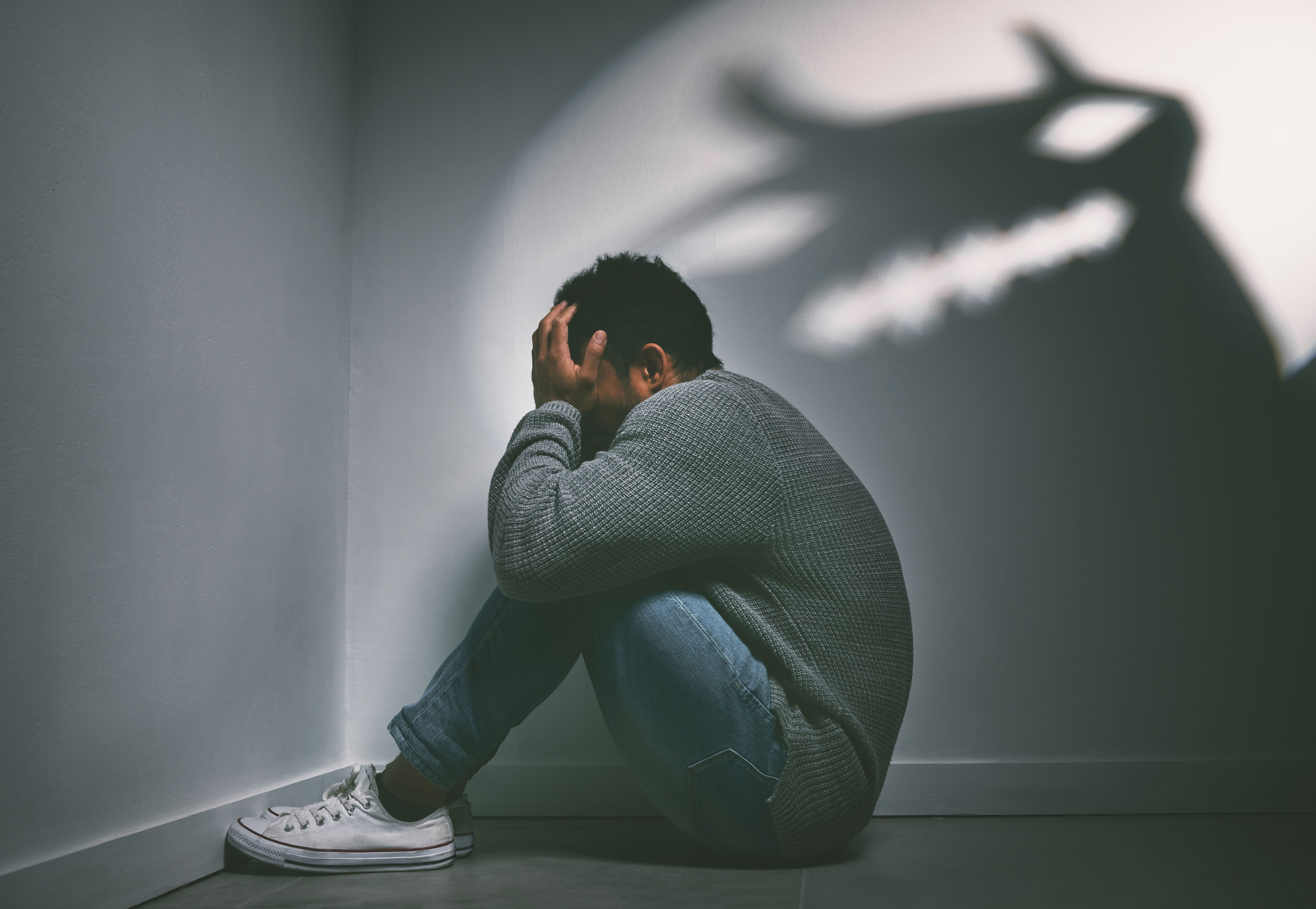 If dreams come true, can nightmares too. Shot of a young man sitting in the corner of a dark room with a scary figure on the wall - Image credit: Siphosethu Fanti/peopleimages.com | stock.adobe.com
