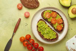 Slices of whole grain rye bread with mashed avocado, green peas and cherry tomatoes seasoned with black sesame seeds are served on a plate for a healthy breakfast or snack