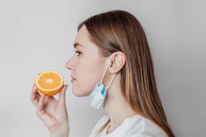 Loss of smell concept. Woman in a medical mask sniffing an orange on a white background in the studio. profile view - Image credit: Evgenia | stock.adobe.com