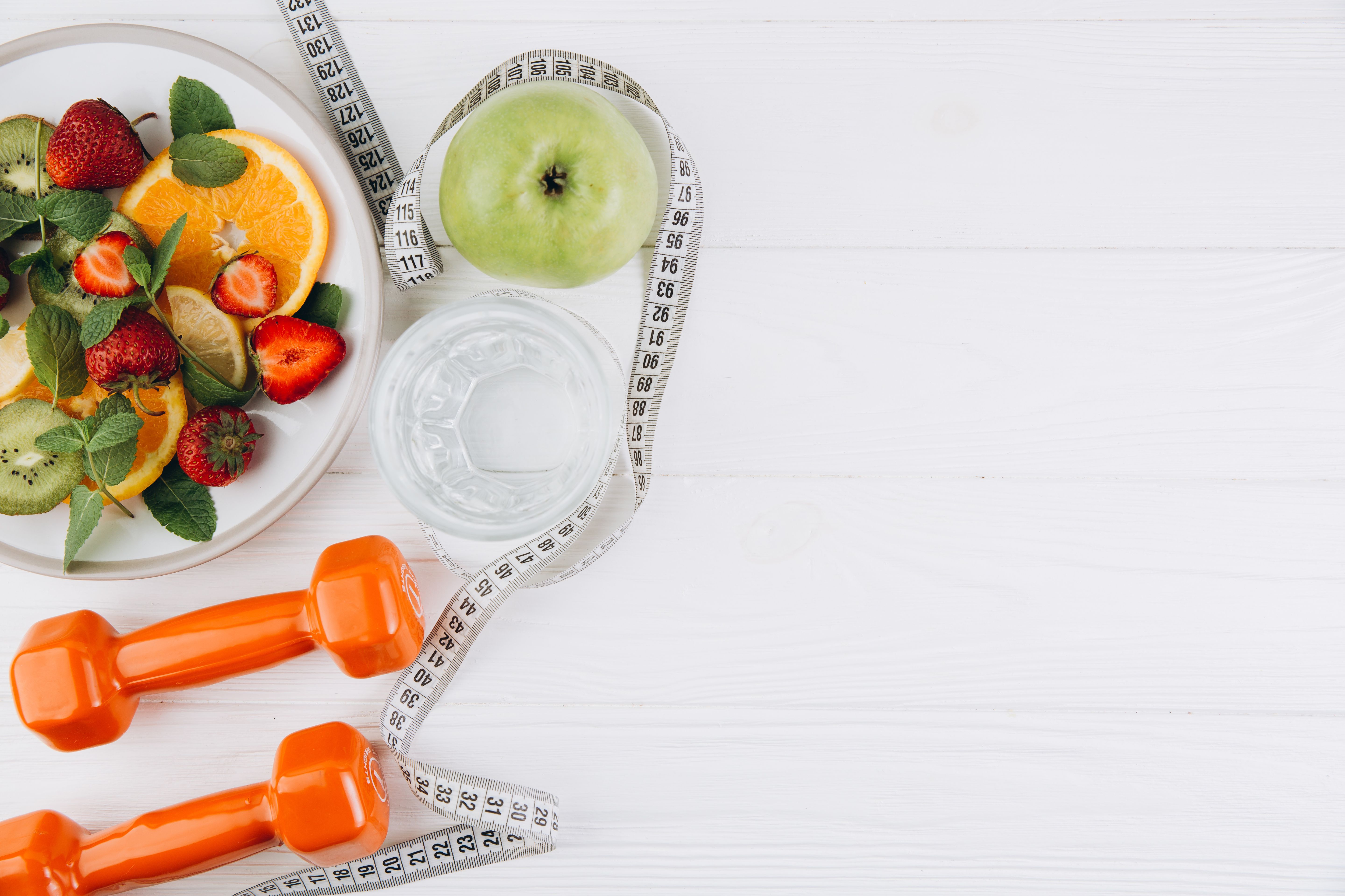 Diet plan, menu or program, tape measure, water, dumbbells and diet food of fresh fruits on white background, weight loss and detox concept, top view - Image credit: anatoliycherkas | stock.adobe.com
