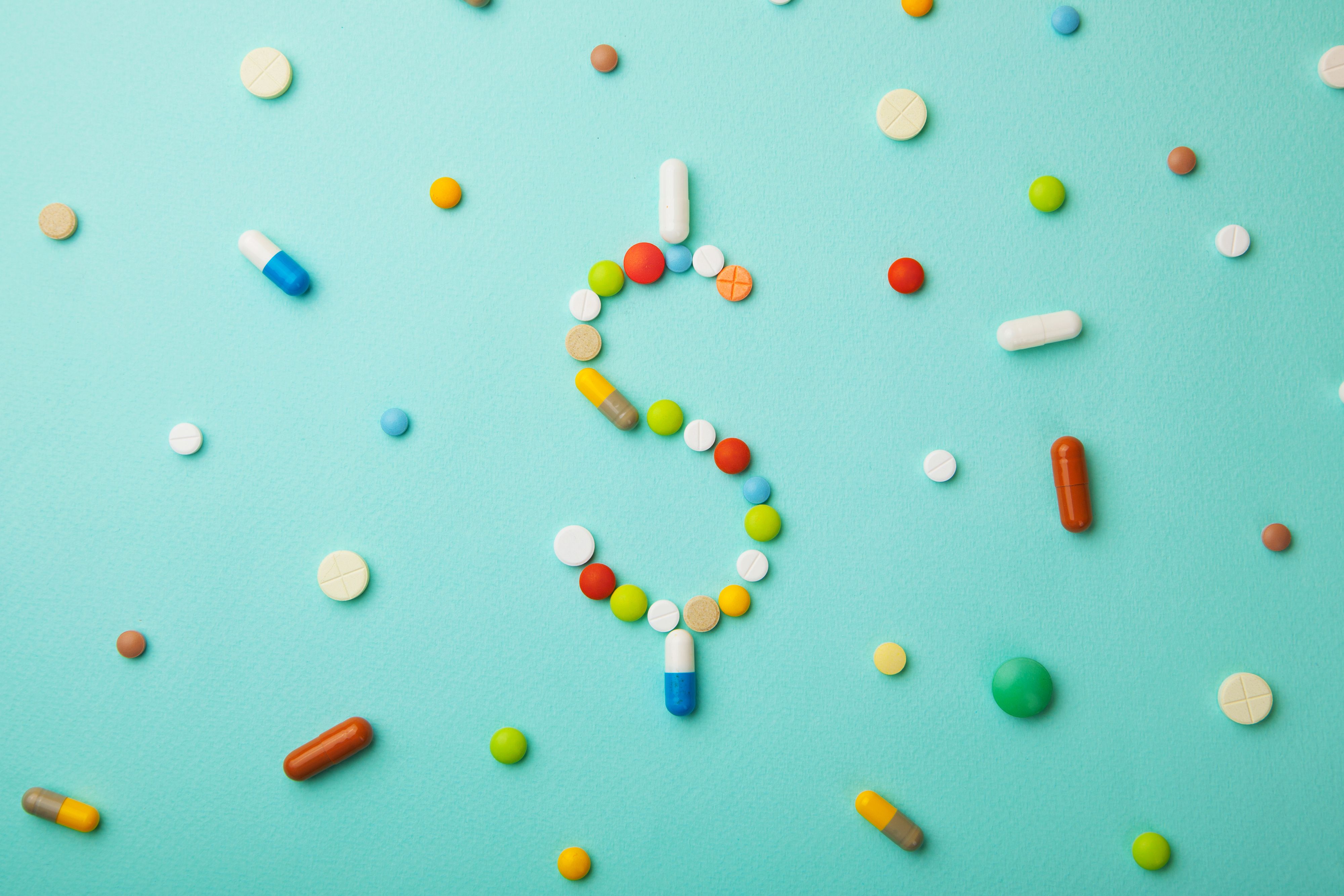 Symbol of money dollar from colored pills and capsules on green background. Expensive medicine and medical insurance. Credit: adragan - stock.adobe.com