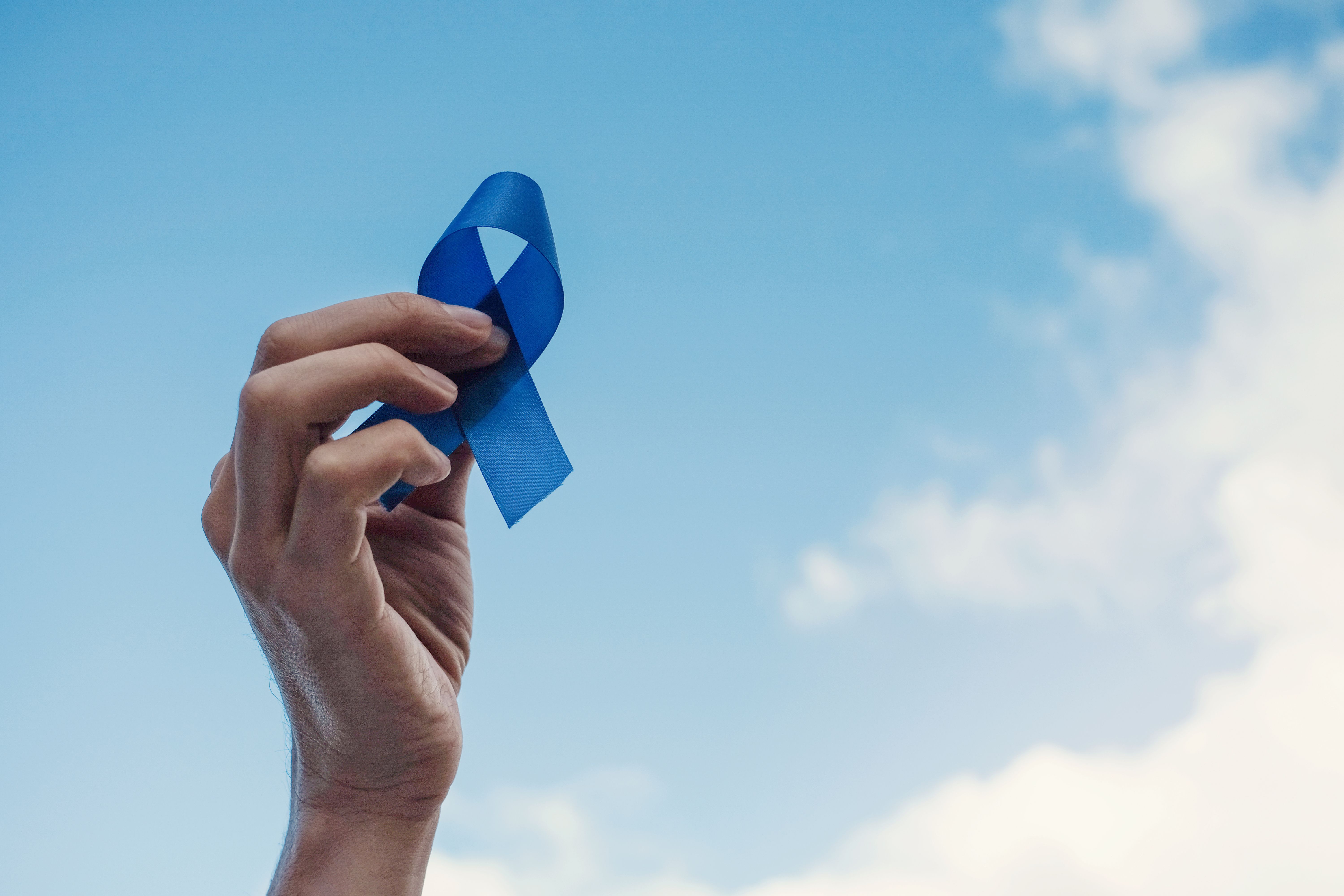 Man holding blue prostate cancer awareness ribbon to the sky | Image Credit: © SewcreamStudio - stock.adobe.com