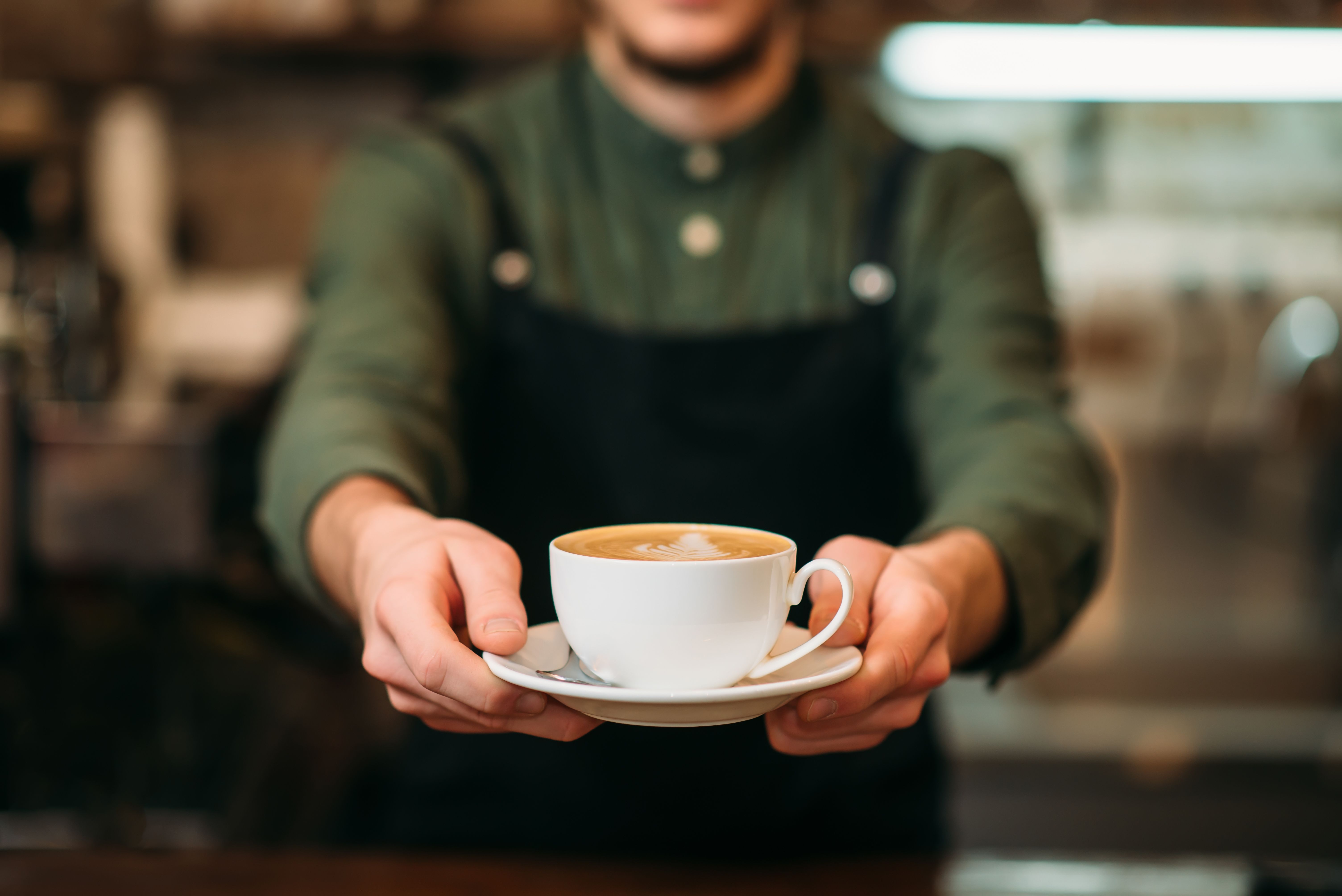 Waiter in black apron stretches a cup of coffee - Image credit: Nomad_Soul | stock.adobe.com