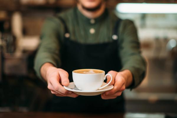 Waiter in black apron stretches a cup of coffee - Image credit: Nomad_Soul | stock.adobe.com