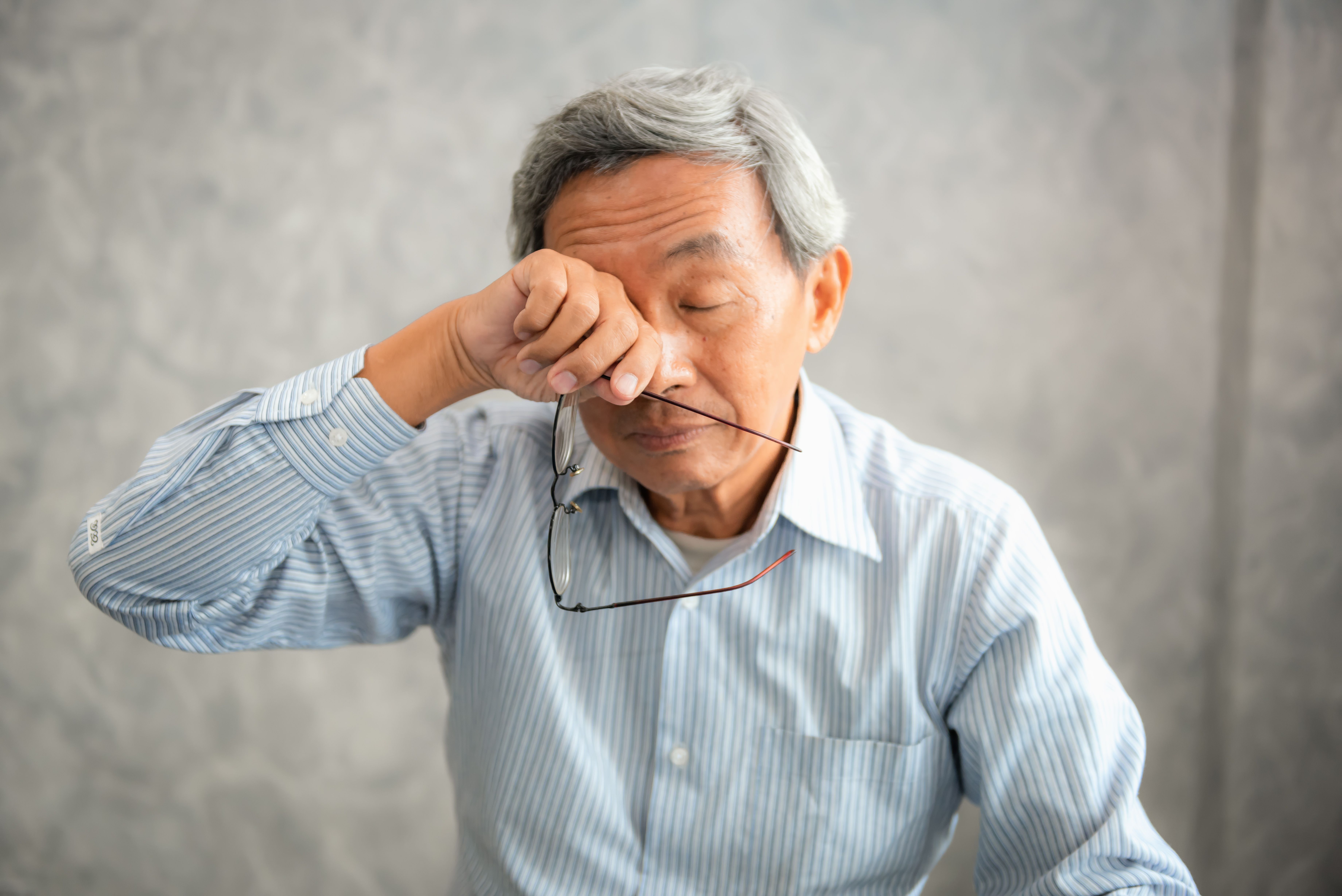 Senior man is holding eyeglasses and rubbing his eyes.