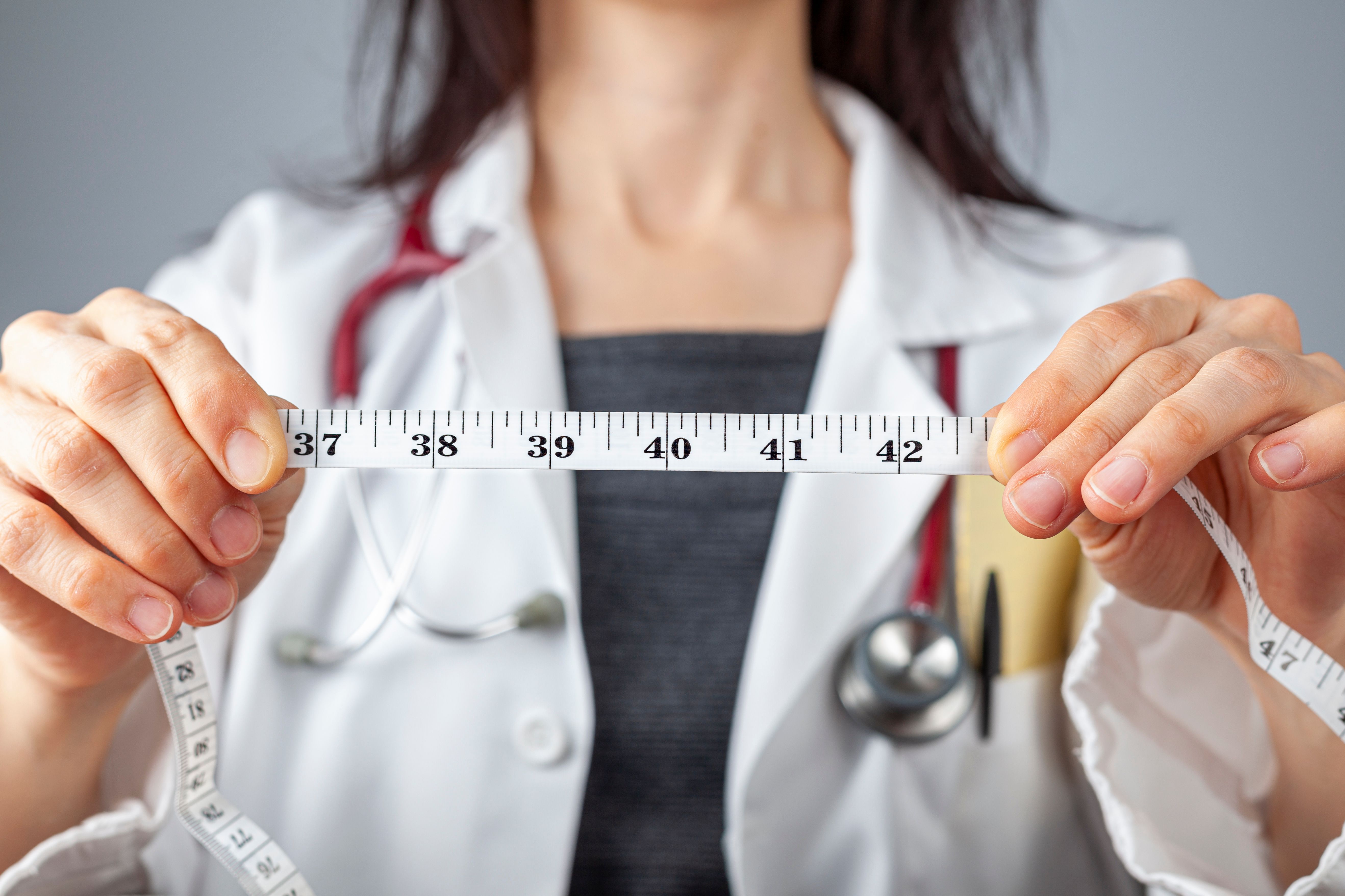 Close up isolated image of a doctor holding a tape measure in her hands which shows 40 inches as abdominal circumference upper limit in healthy people. Concept for weigh loss and fitness. | Image Credit: Grandbrothers | stock.adobe.com