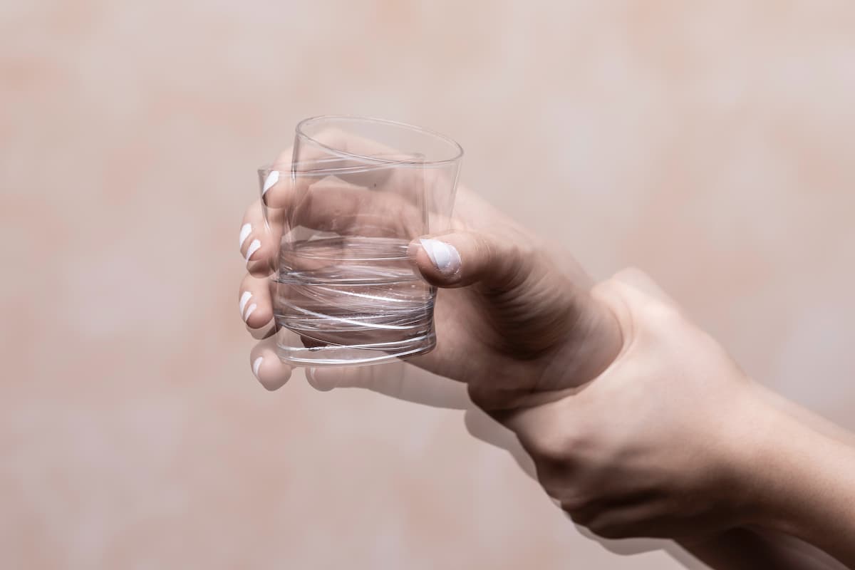 Trembling hand holding glass with alcohol drink