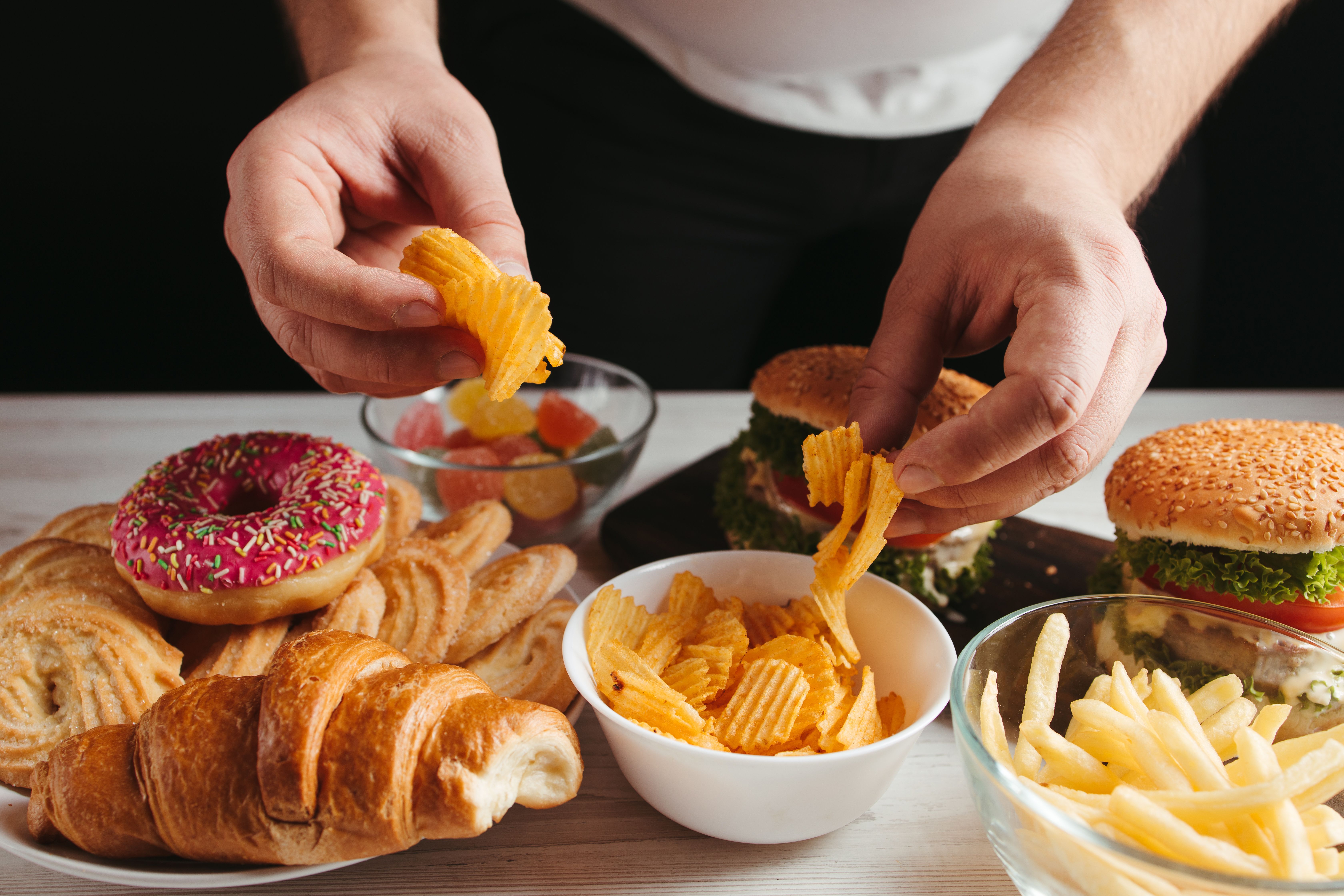 Person grabbing chips from bowl surrounded by other ultraprocessed foods | Image Credit: © Vadym - stock.adobe.com
