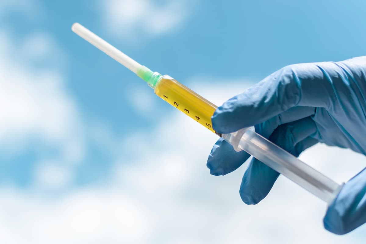 Blood plasma as a hope for treatment of coronavirus infection. Syringe with blood plasma in a hand in a blue medical glove against the sky. Platelet-Rich plasma preparation.