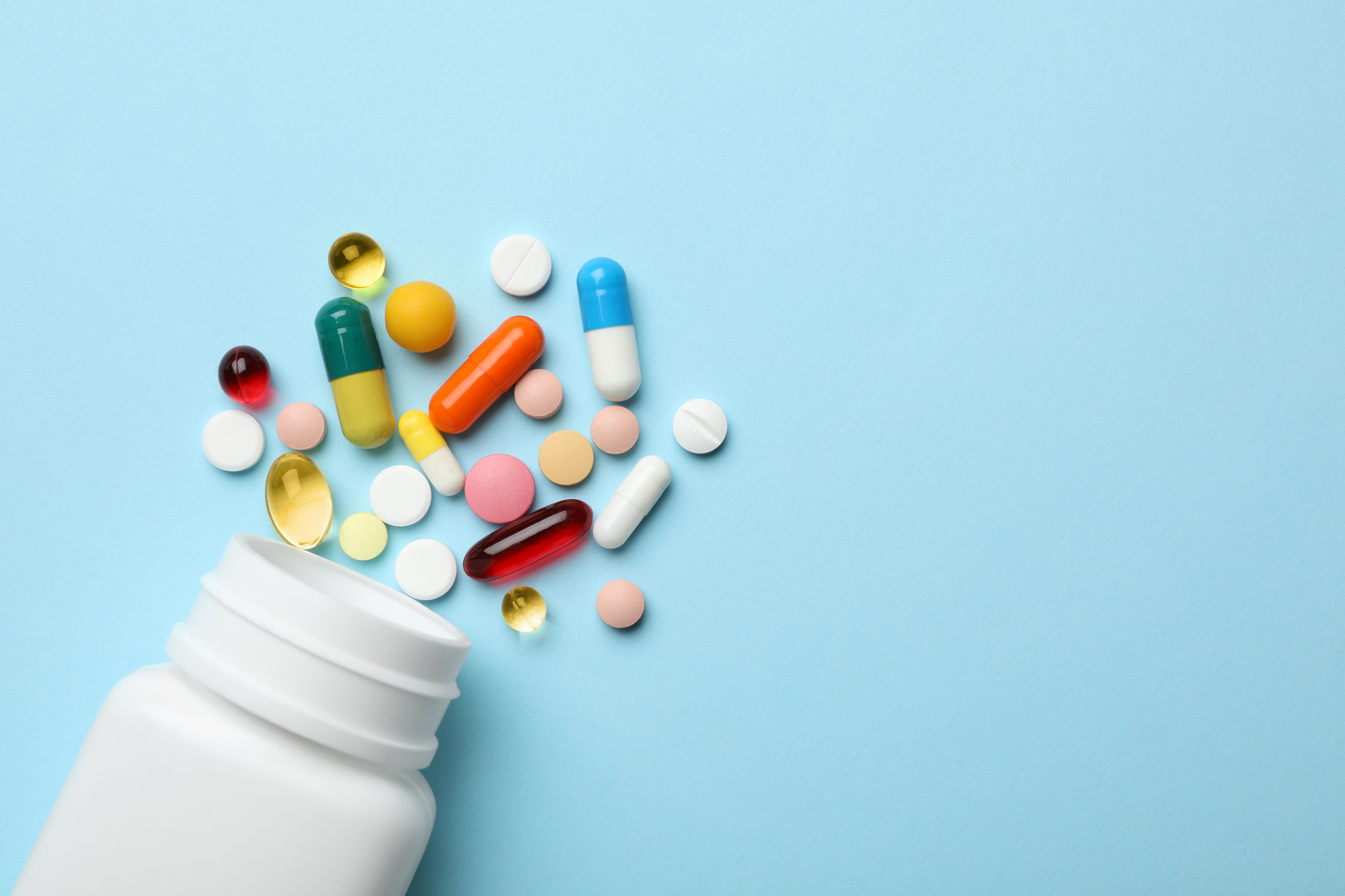 Bottle and scattered pills on color background, top view. Space for text - Image credit: New Africa | stock.adobe.com
