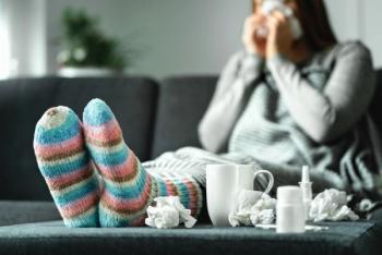 Sick woman with flu, cold, fever and cough sitting on couch at home. Ill person blowing nose and sneezing with tissue and handkerchief. Woolen socks and medicine. Infection in winter. Resting on sofa - Image credit: terovesalainen | stock.adobe.com 