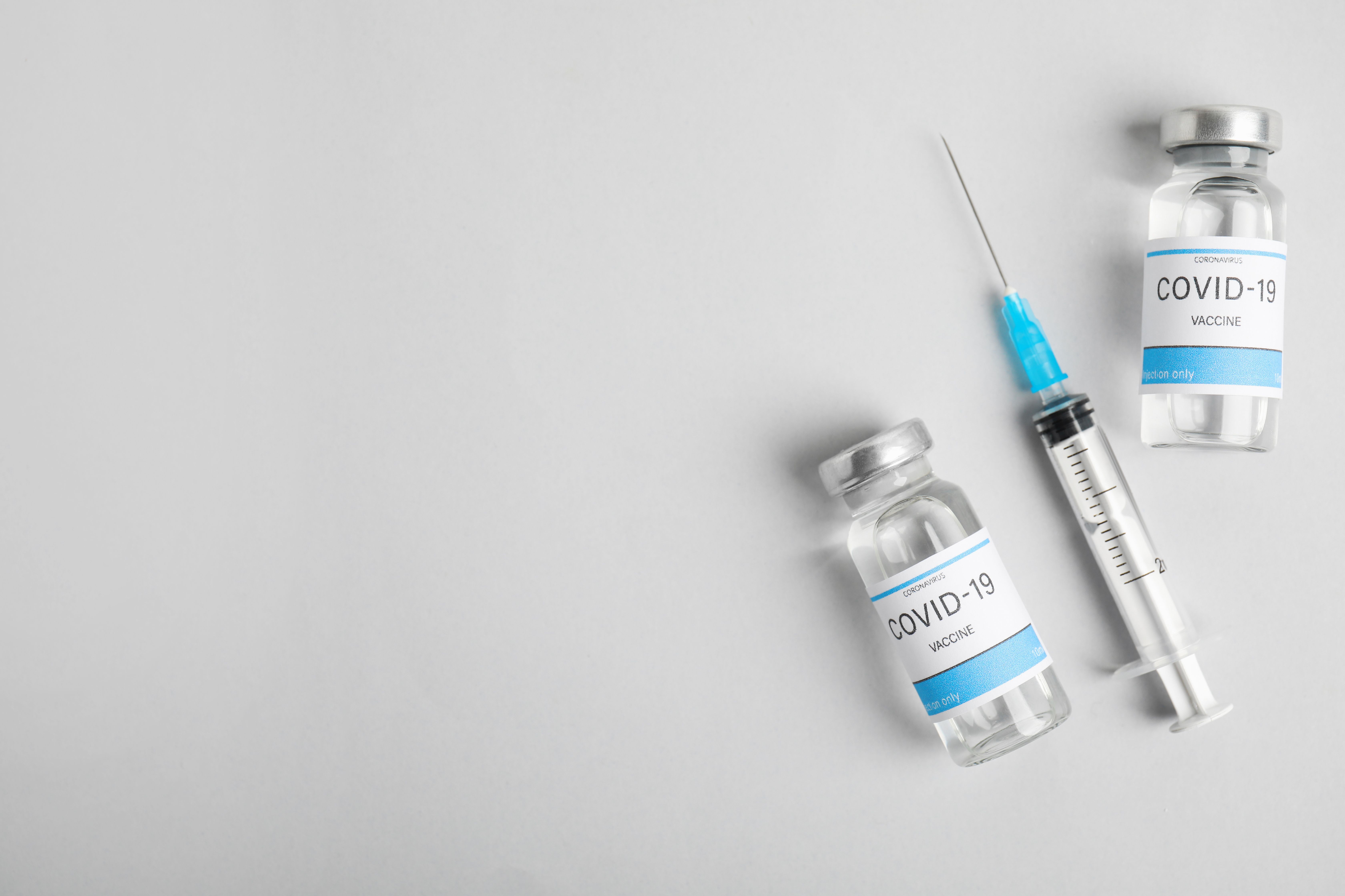 Vials with coronavirus vaccine and syringe on light background, flat lay- Image credit: New Africa | stock.adobe.com