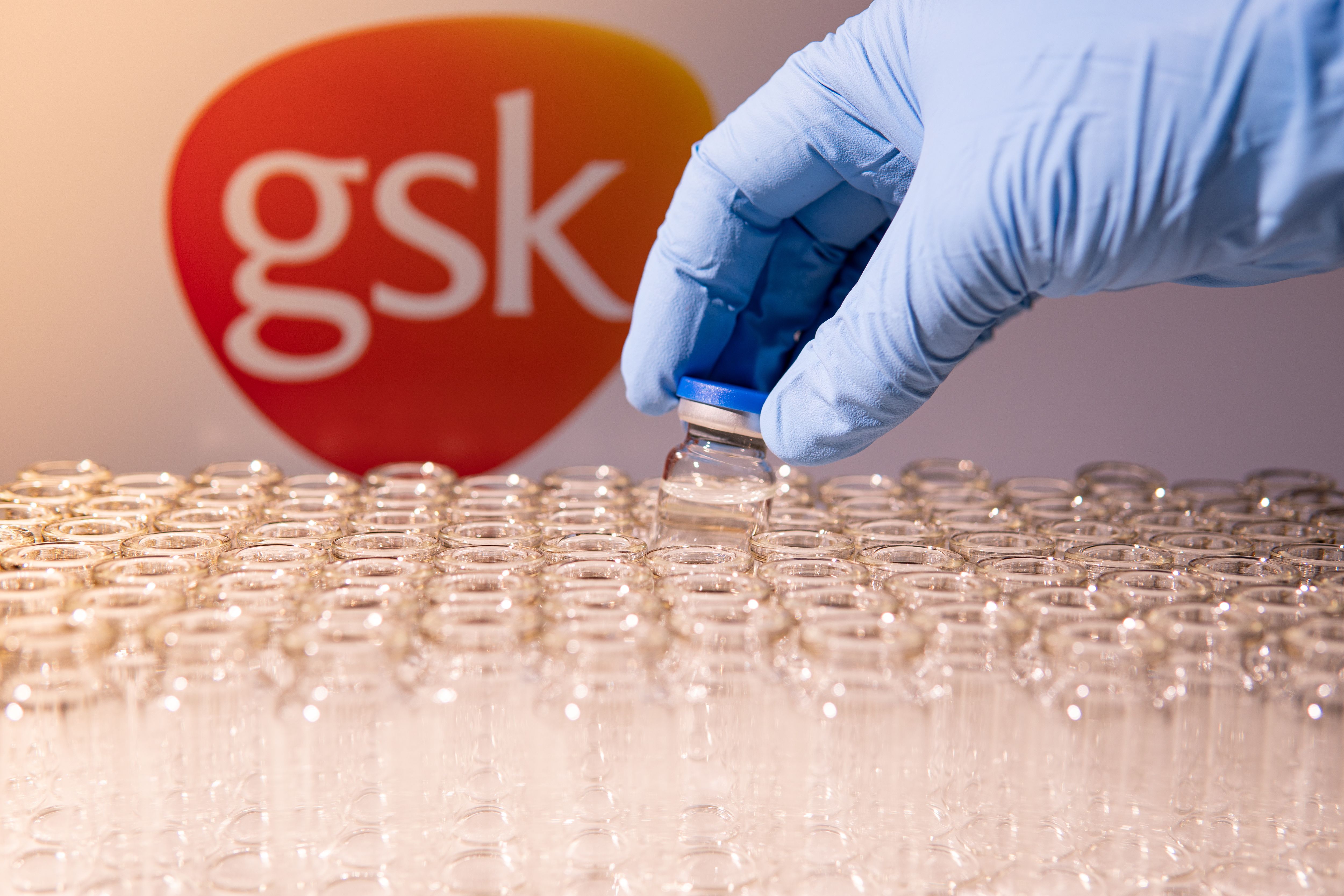 Scientist holding the glass vial, GSK blurred in background | Image Credit: © desertsands - stock.adobe.com