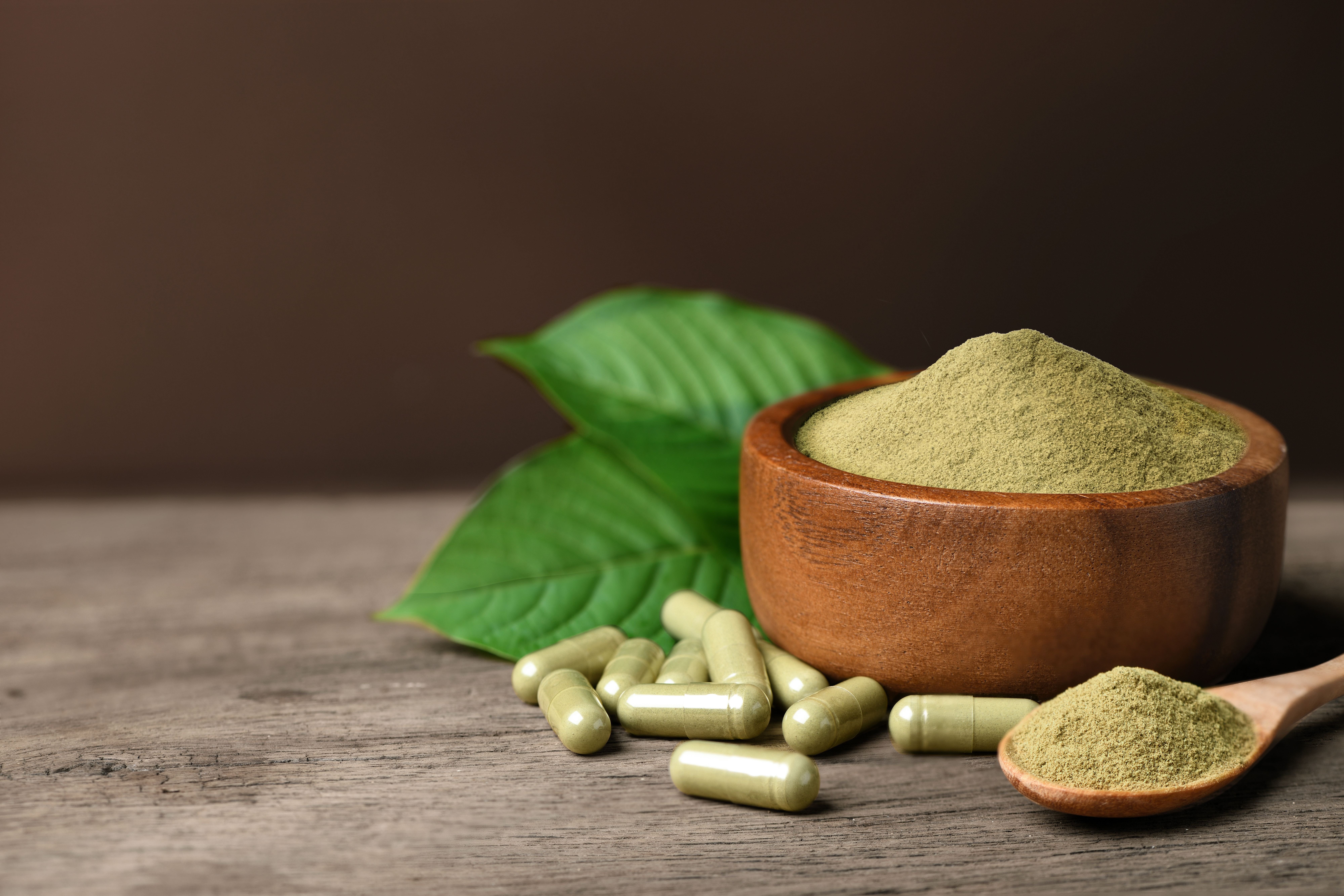 Kratom (Mitragyna speciosa) capsules with powder and fresh leaf on wood background. | Image Credit: Paitoon | stock.adobe.com 