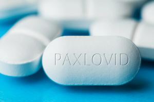 Uzice, SERBIA - Dec 22nd 2021: A pile of Pfizer PAXLOVID antiviral drug pills on blue background,cure for Coronavirus infection,COVID-19 virus disease prevention and protection, illustration