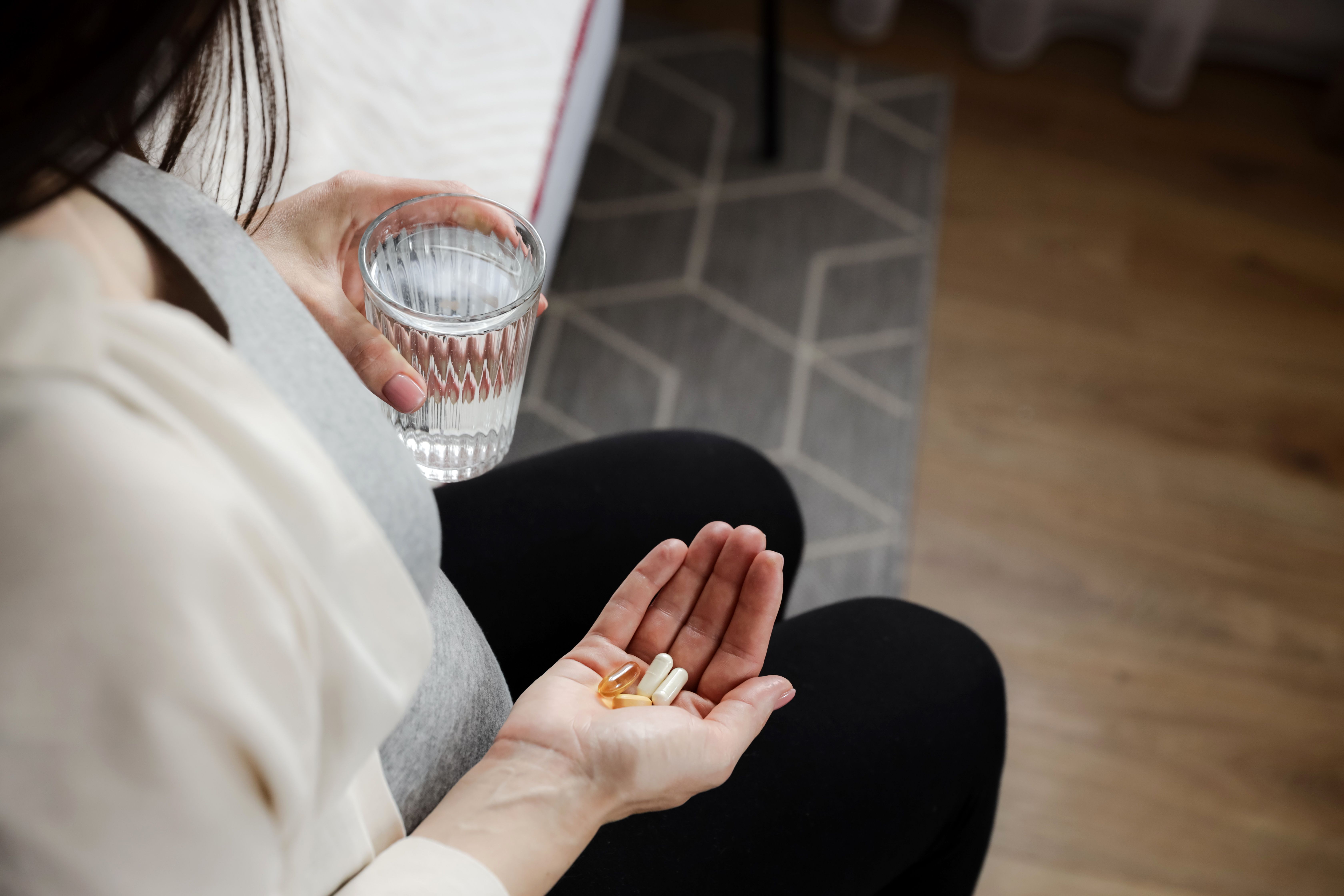 Close up of pregnant woman holding glass of water and heap of pills in hand, taking vitamins D, E, A, calcium, dietary supplements, omega 3 in fish oil capsules at home. Pregnancy, prenatal health - Image credit: Lena Ivanova | stock.adobe.com