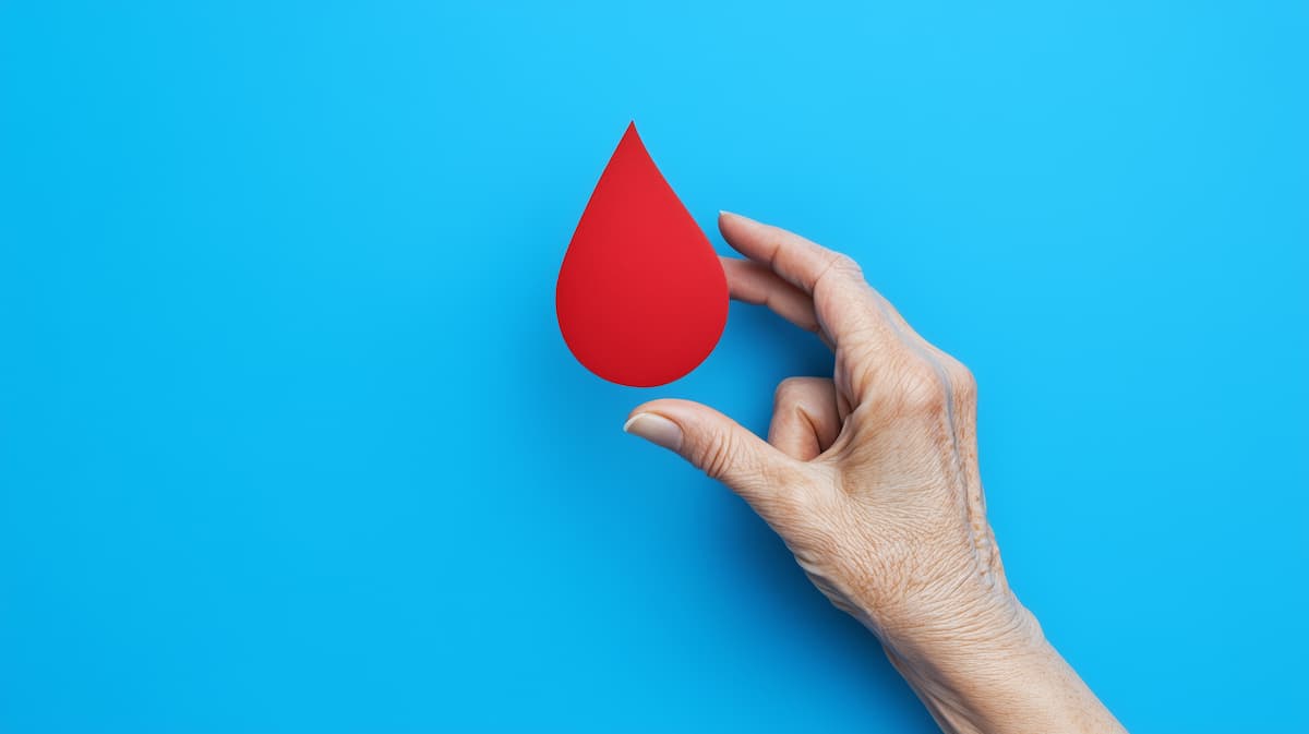 World hemophilia day concept with red blood drop symbol and elder hand on blue background with copy space.