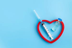 Heart Injection And Vaccine Vial. Covid 19 Cure. Medical Ampoule Dose And Needle On Blue Background, Top View With Copy Space - Image credit: Polina Zait | stock.adobe.com