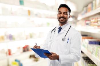 medicine, pharmacy and healthcare concept - smiling indian male doctor or pharmacist in white coat with stethoscope and clipboard over drugstore background - Image credit: Syda Productions | stock.adobe.com