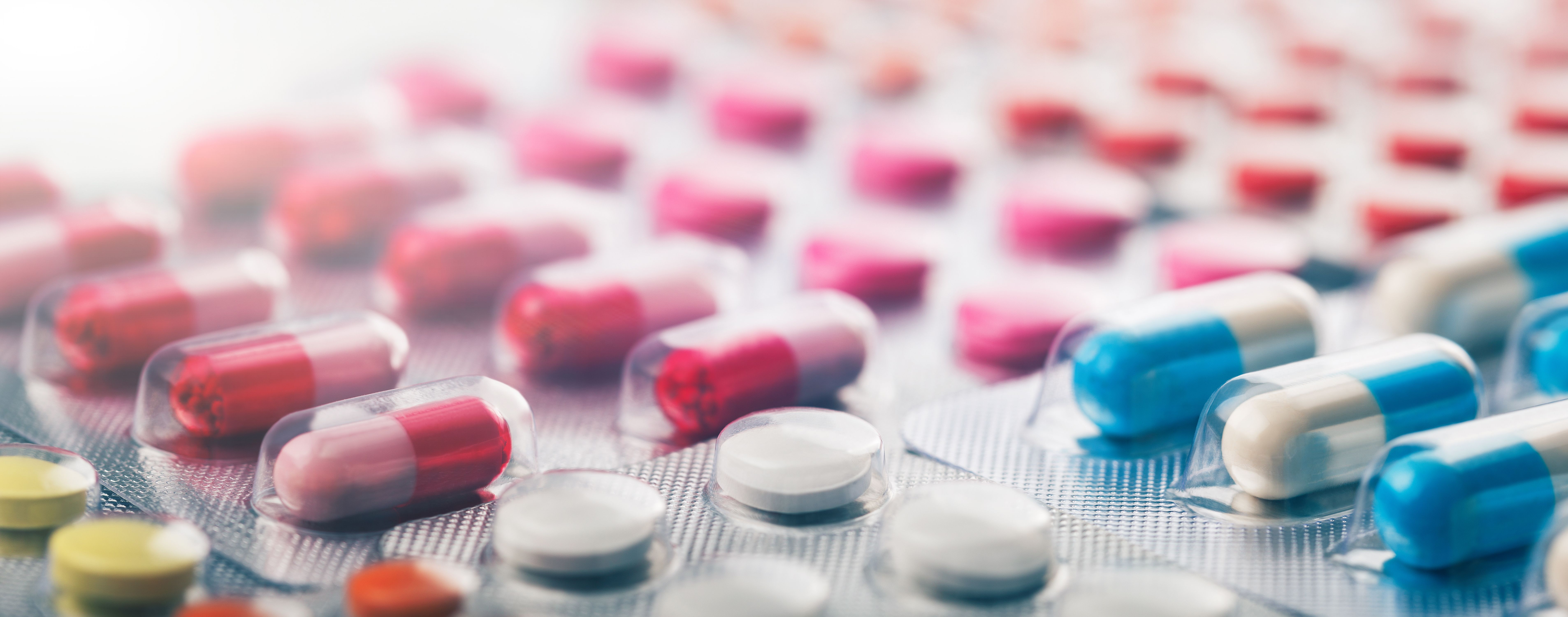 Heap of medical pills in white, blue and other colors. Pills in plastic package. Panoramic banner for design. | Image Credit: okskaz | stock.adobe.com