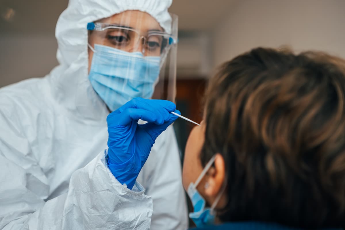 Close up of female health Professional in PPE introducing a nasal swab to a senior female patient