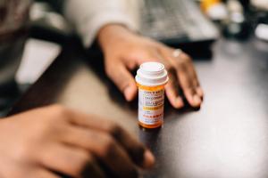 Man taking opioid pills sitting at a dark table - Image credit: rohane | stock.adobe.com