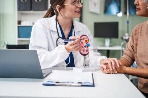 Caucasian woman and elderly Asian woman discuss kidney model issues like gallstones, glomerulonephritis, acute/chronic kidney disease, infections, abnormal ureters, cysts, urinary system ..