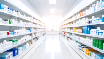 Blurred shelves filled with various medical products in a pharmacy background, highlighting healthcare supplies, pharmaceutical items, medicine packaging, and clinical retail environment. | Image Credit: CreativeArs | stock.adobe.com